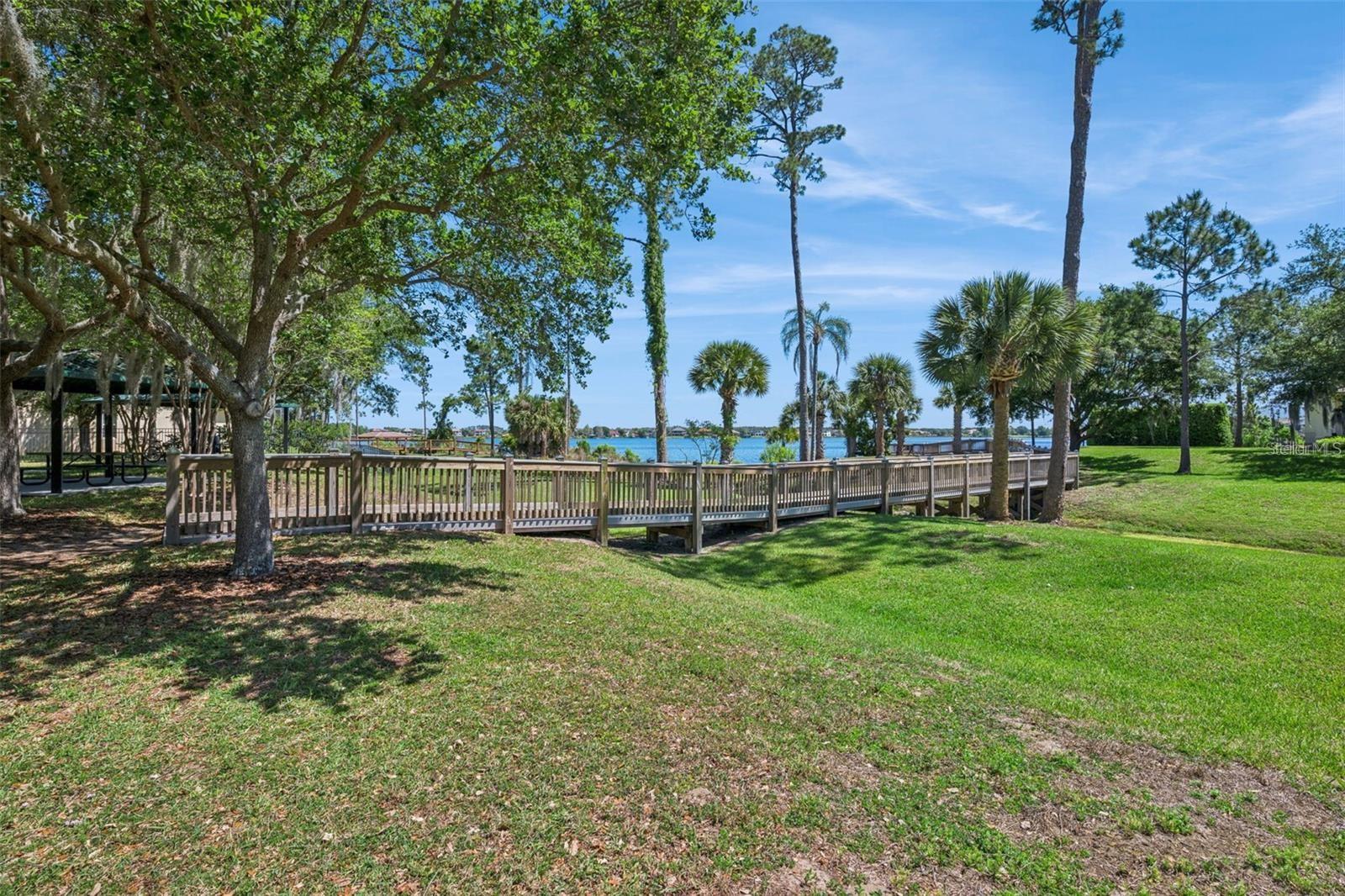 Waterfront grounds with a wooden boardwalk, grassy lawn, mature trees, and a lake view.