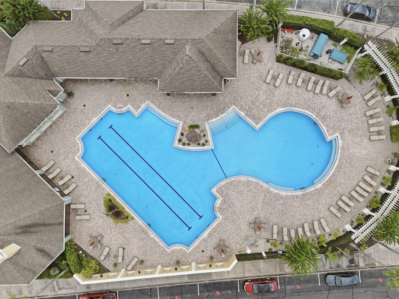 Aerial view of a curving community pool surrounded by lounge chairs and a paved deck.