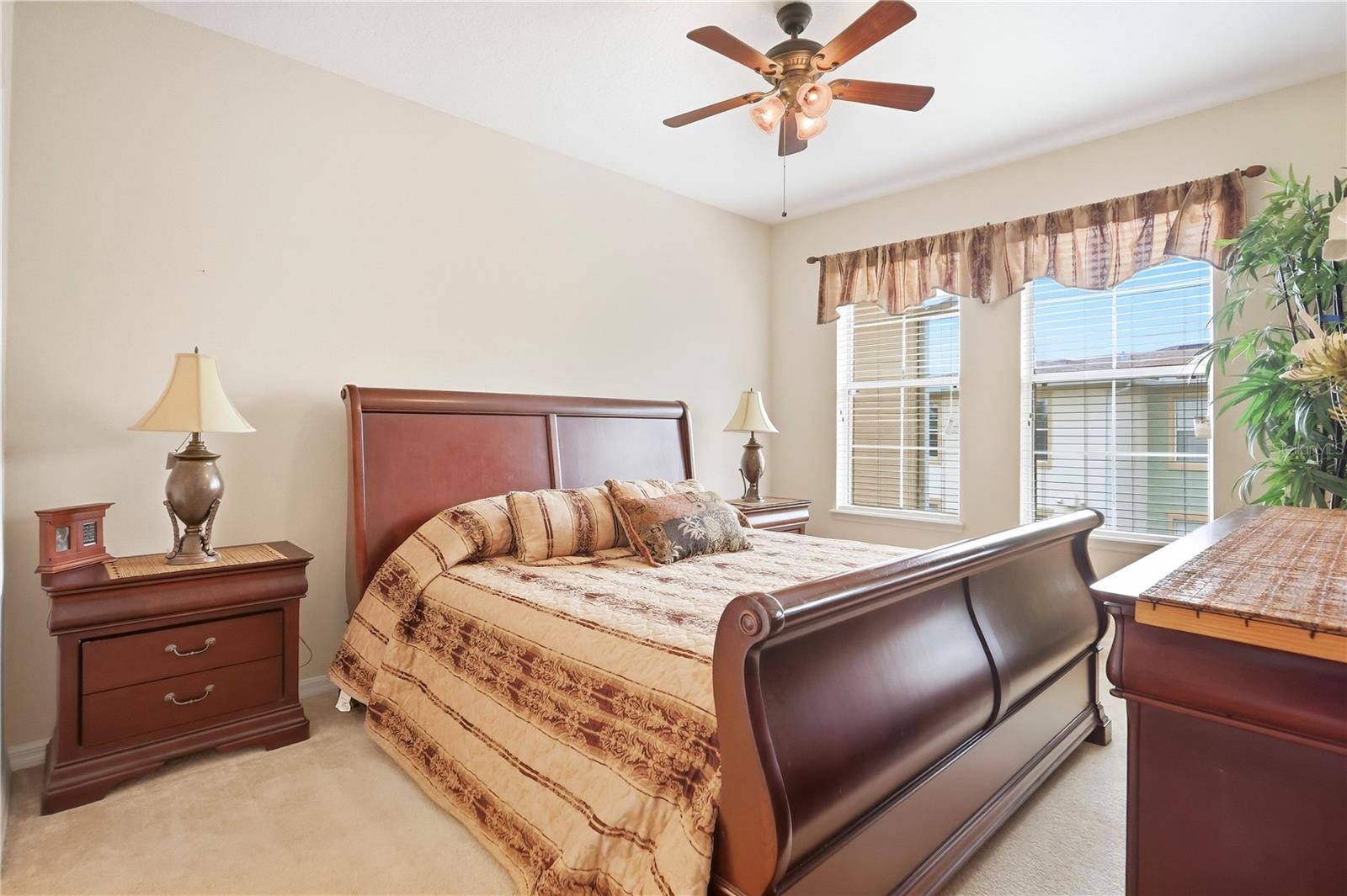 Furnished bedroom with a dark wood sleigh bed, patterned bedding, and two windows with blinds.