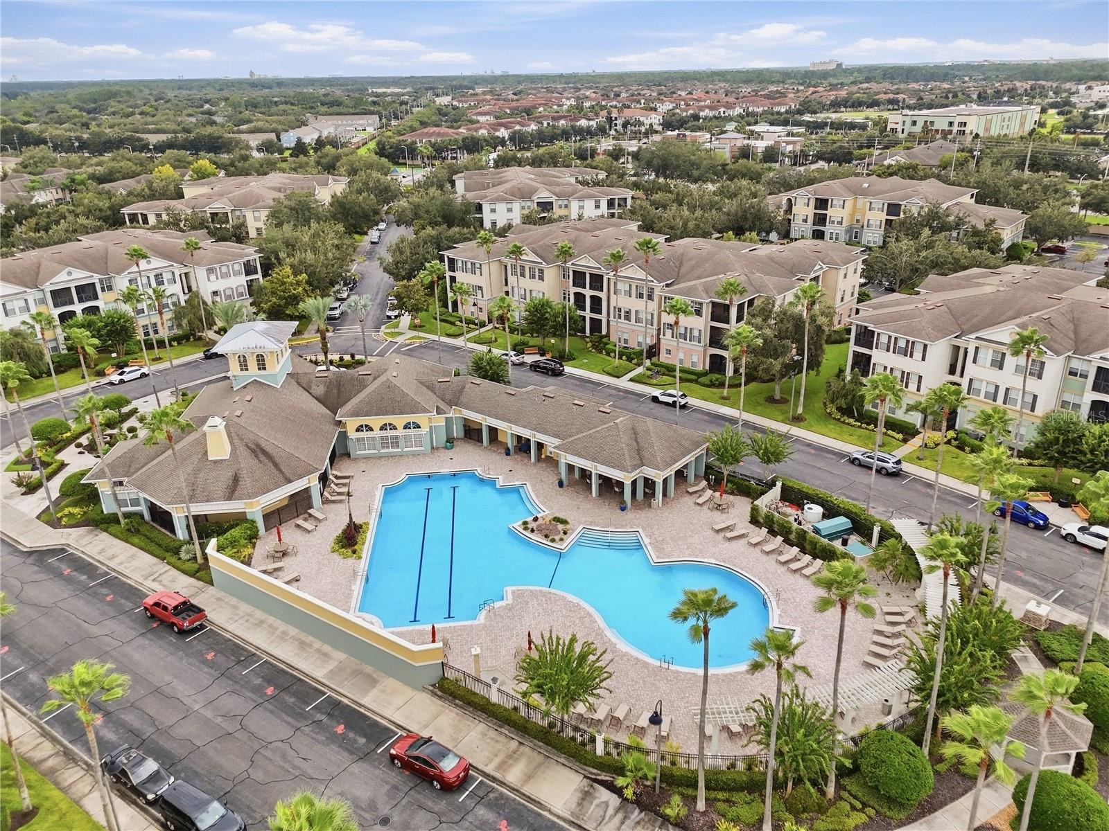 Aerial view of a condominium community with a large swimming pool and palm-lined grounds.