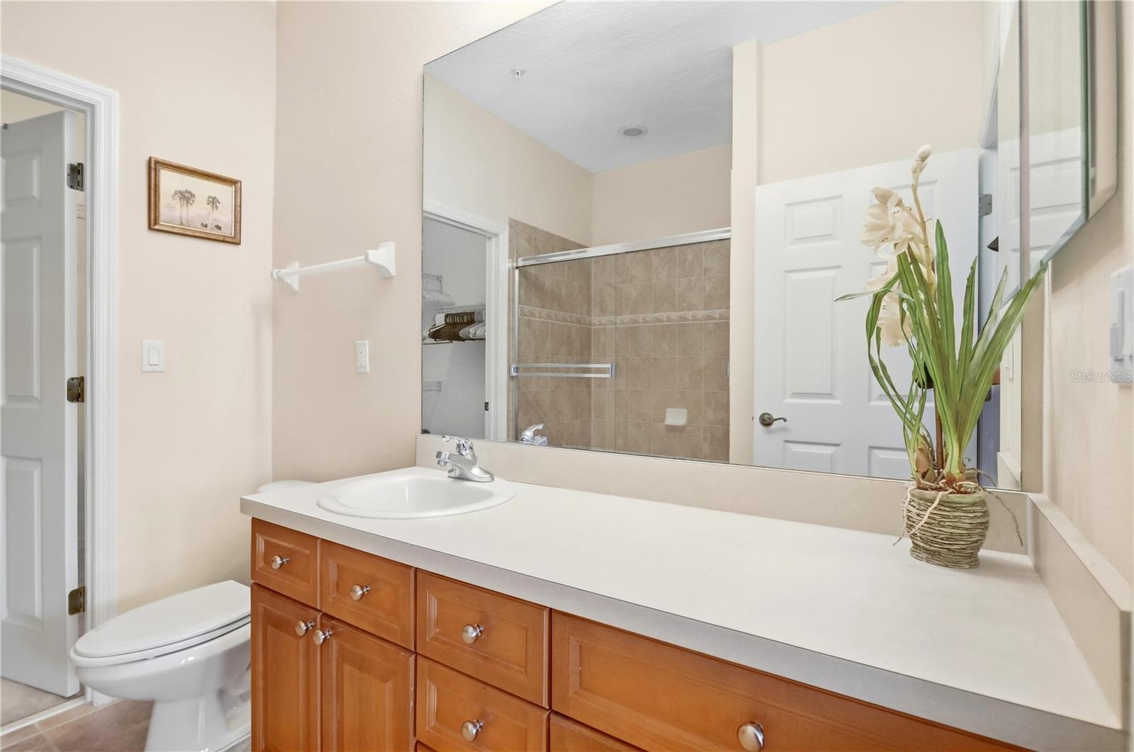 Bathroom with a long wood vanity, white countertop, mirrored wall, and tiled shower.