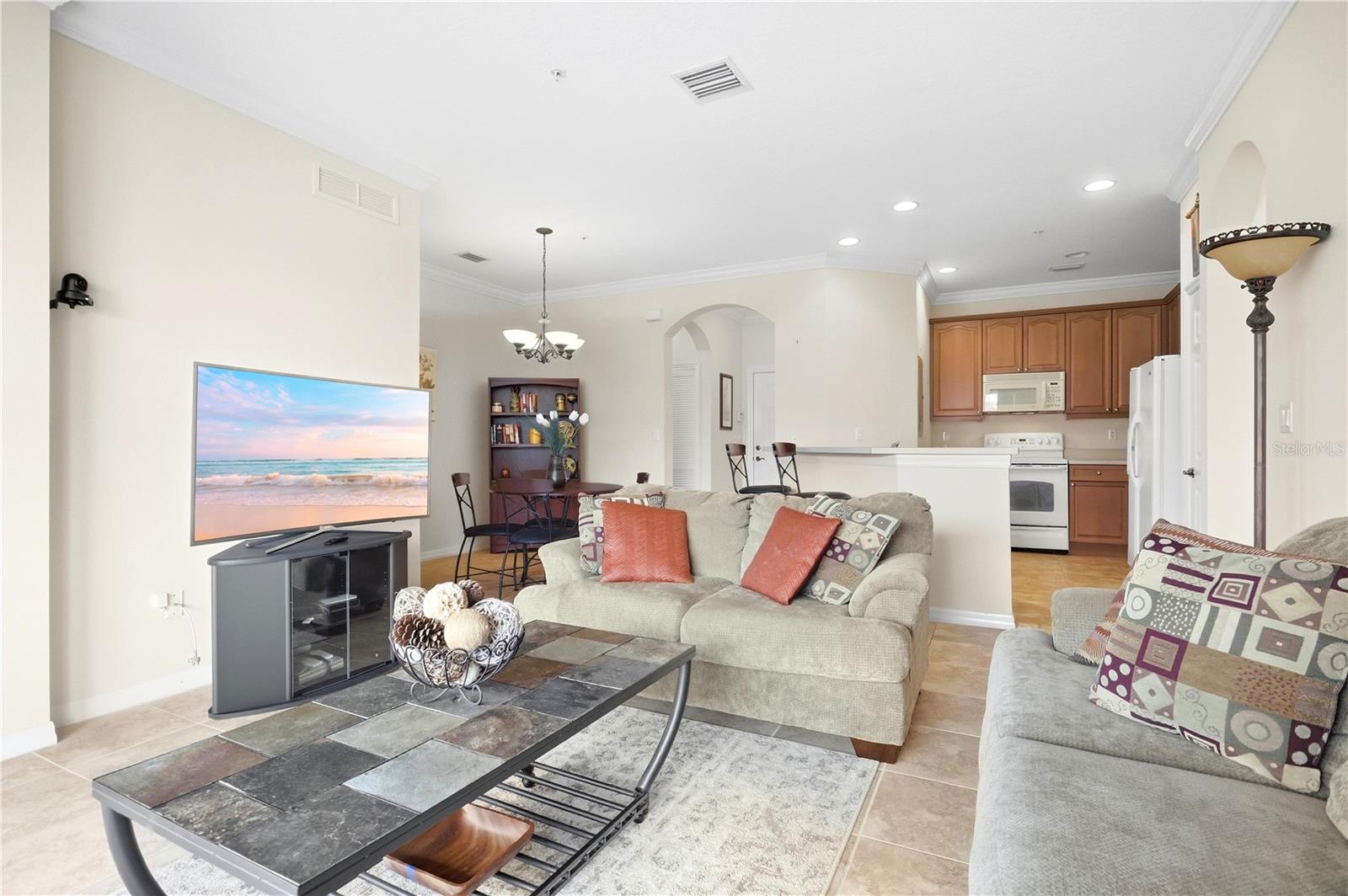 Open-plan living room with beige sofas and a tiled coffee table beside a wood-cabinet kitchen.