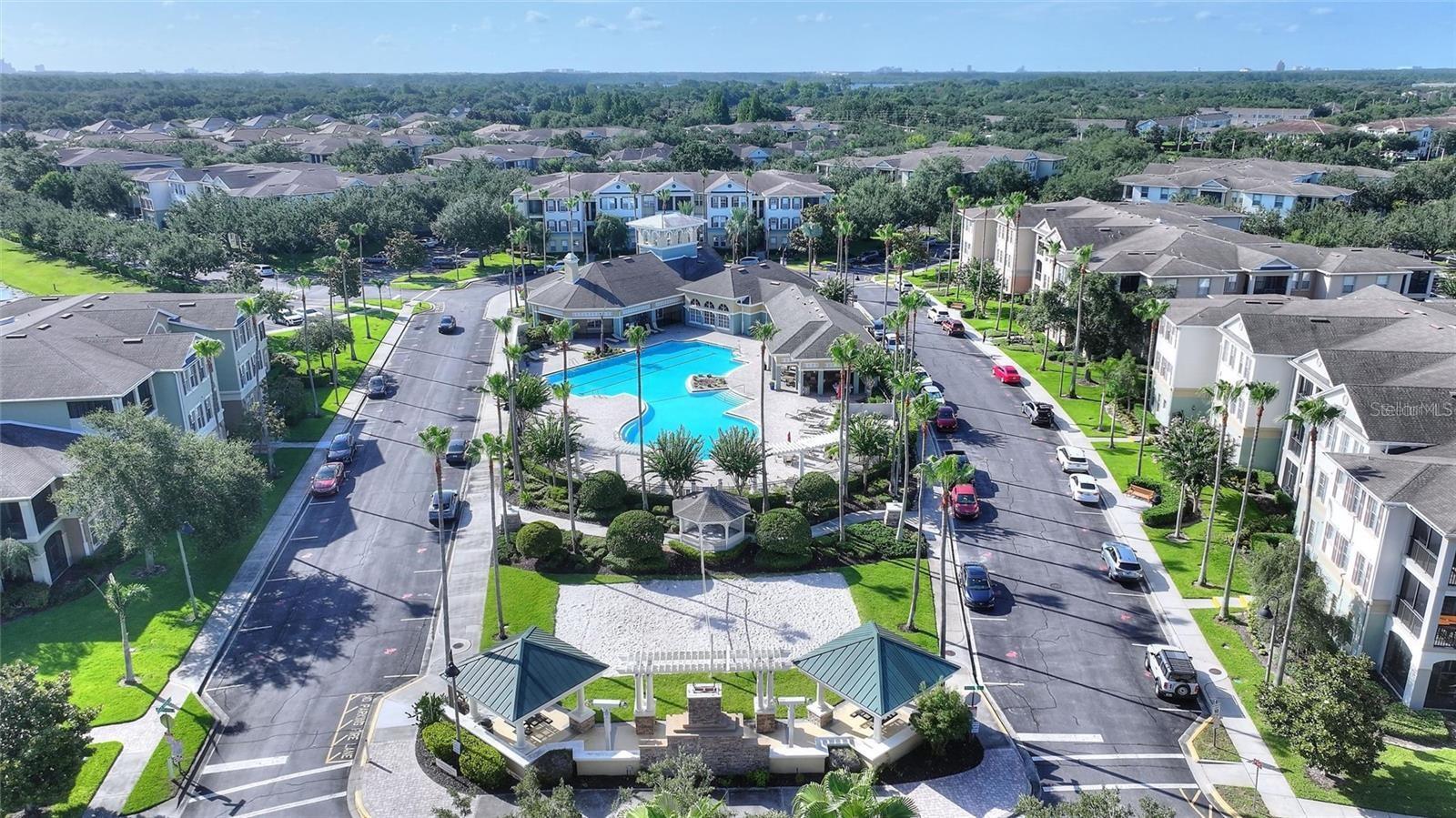 Aerial view of a condominium community centered around a swimming pool and surrounded by palm trees.