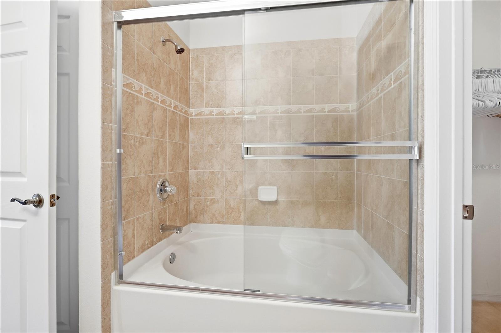 Bathroom with a white tub-shower, clear glass enclosure, and beige tile with a decorative border.
