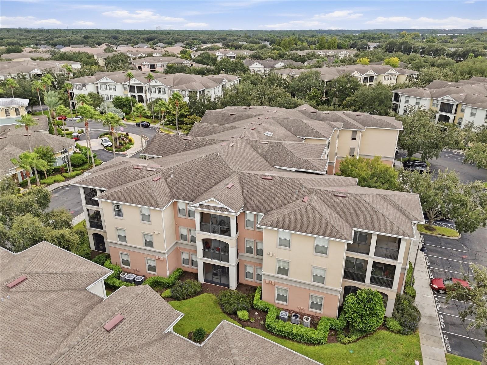Aerial view of apartment buildings with balconies, landscaped grounds, and parking areas.
