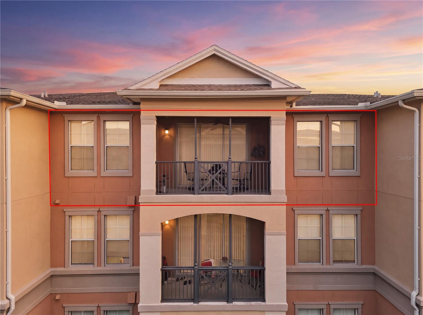 Condominium facade at dusk, with a red outline highlighting an upper-floor unit and its covered balcony.