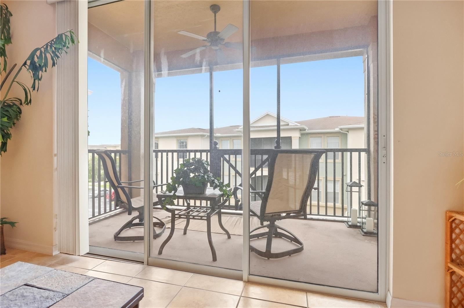 Screened balcony with two swivel chairs and a potted table, viewed through sliding glass doors.