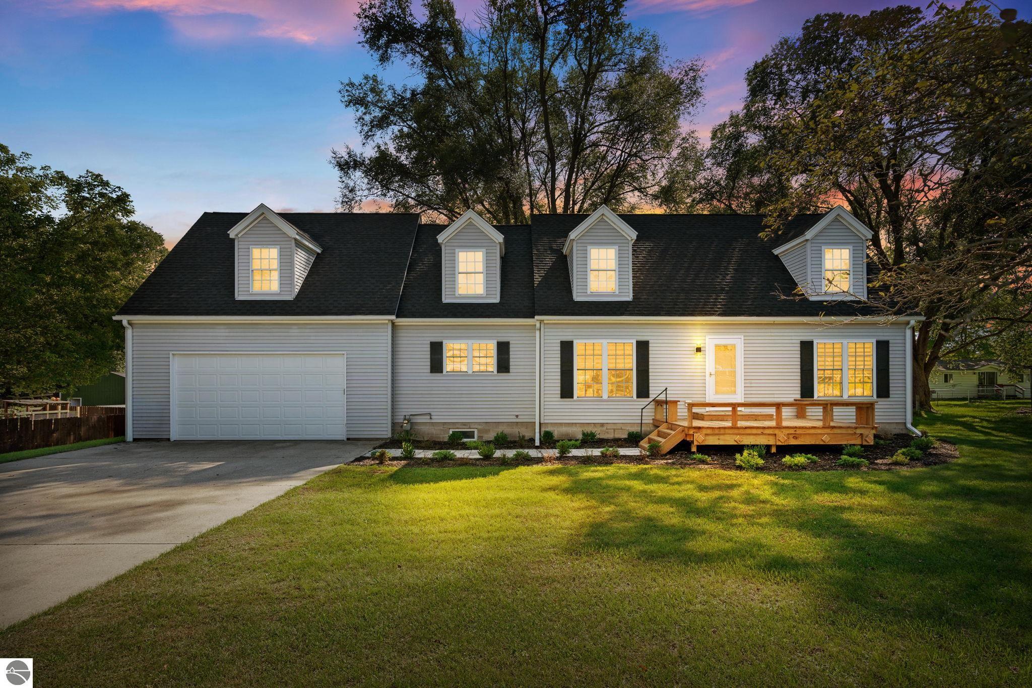 Gray two-story home with four dormers, an attached garage, and a wooden front porch at dusk.