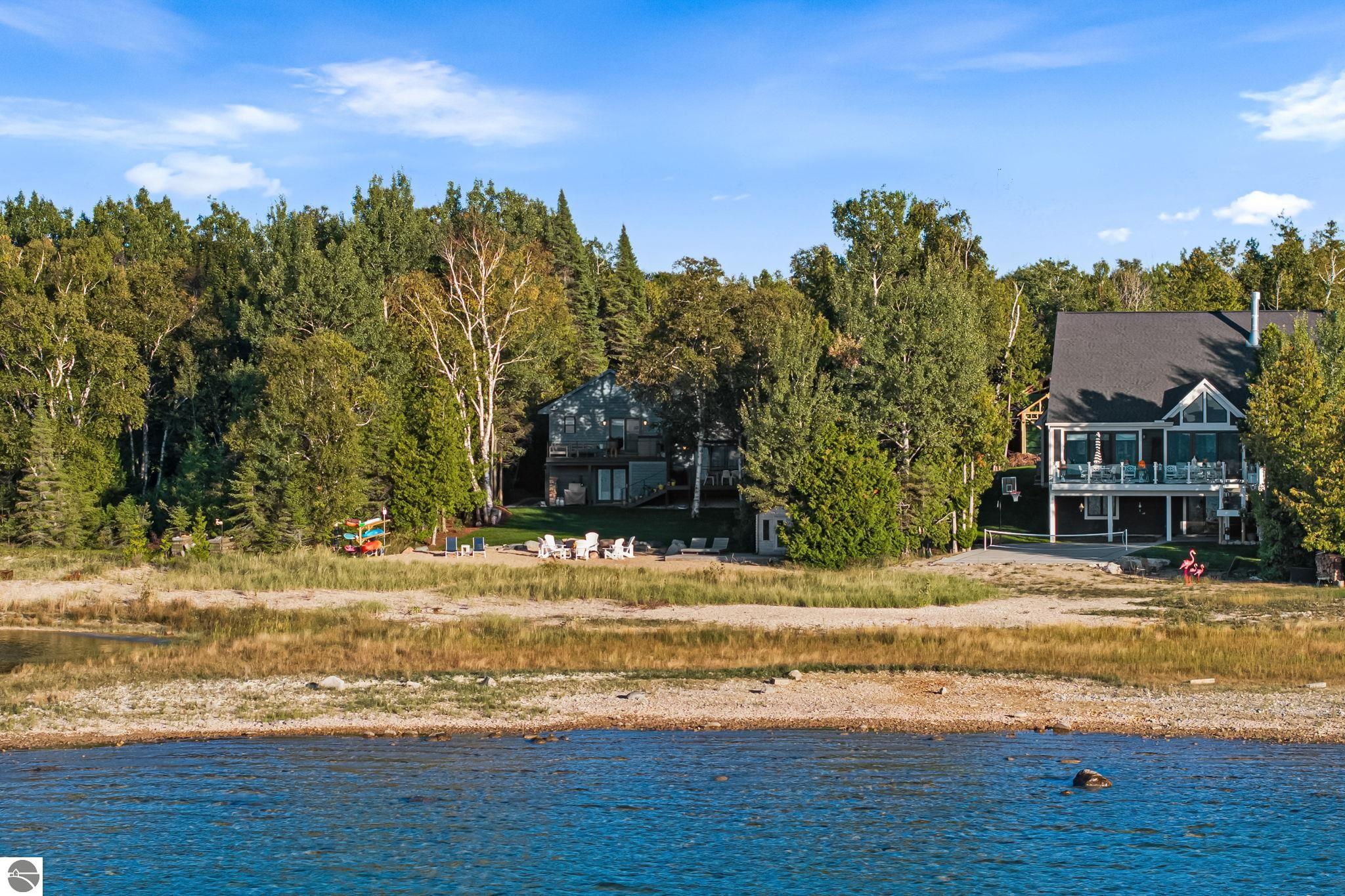 Two modern homes among trees on a rocky lakeshore across blue water.