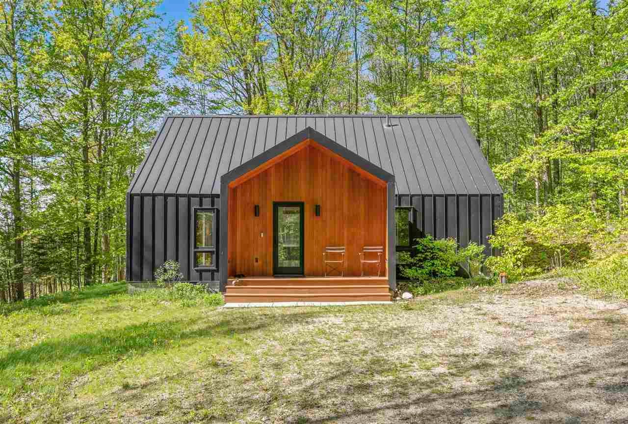 Modern dark metal-sided home with a warm wood entry porch, surrounded by leafy trees.