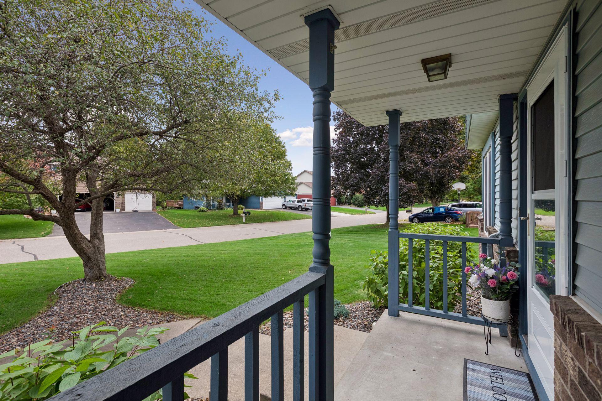 Covered front porch with dark blue railings overlooks a leafy lawn and neighborhood street.
