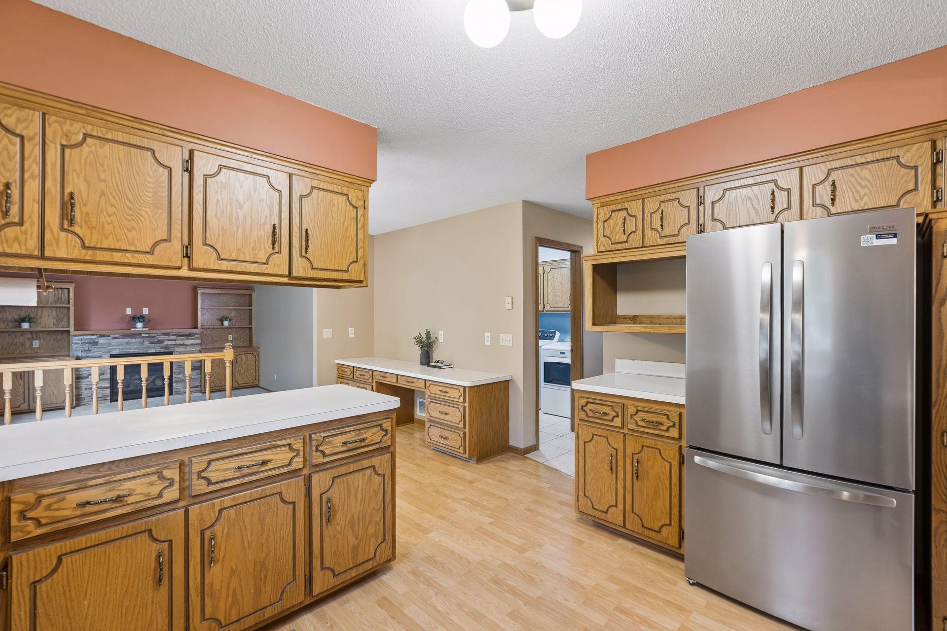 Kitchen with ornate oak cabinetry, white counters, a large island, and stainless steel refrigerator.