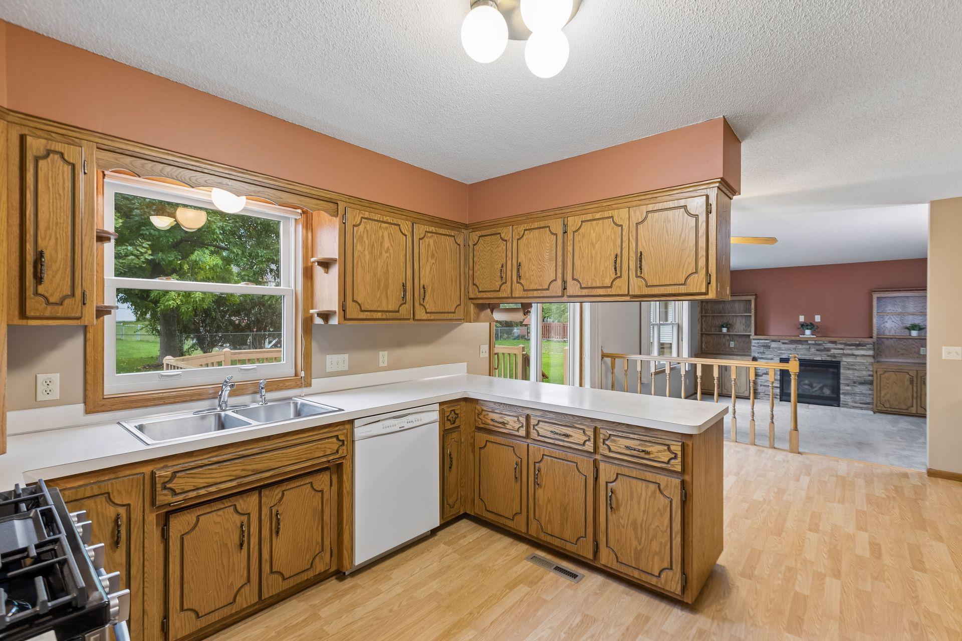 Kitchen with oak cabinets, white countertops, and a window above the sink, opening to a living area.