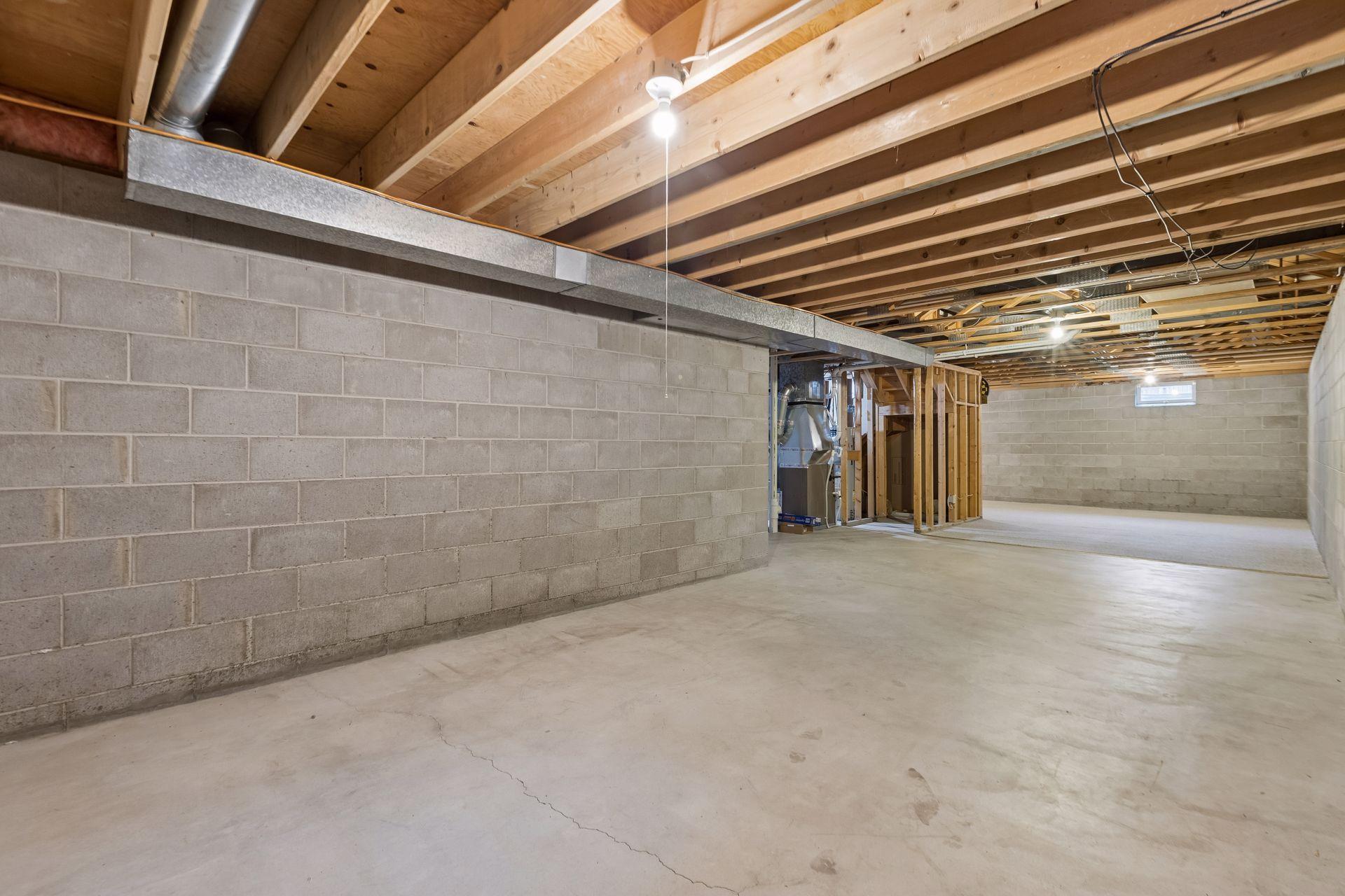 Unfinished basement with exposed ceiling joists, concrete block walls, and open floor space.