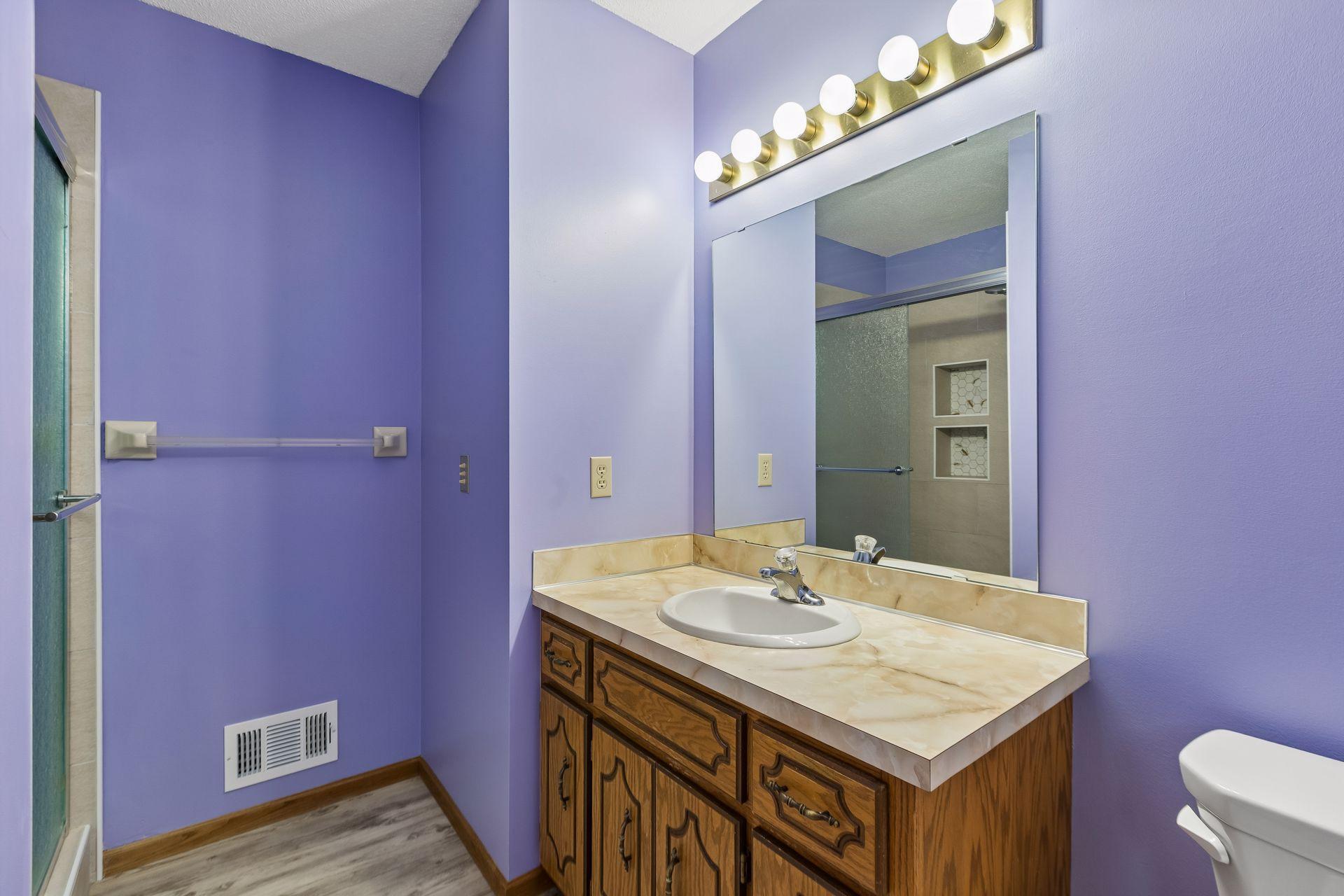 Bathroom with lavender walls, a wood vanity, and a large mirror above the sink.