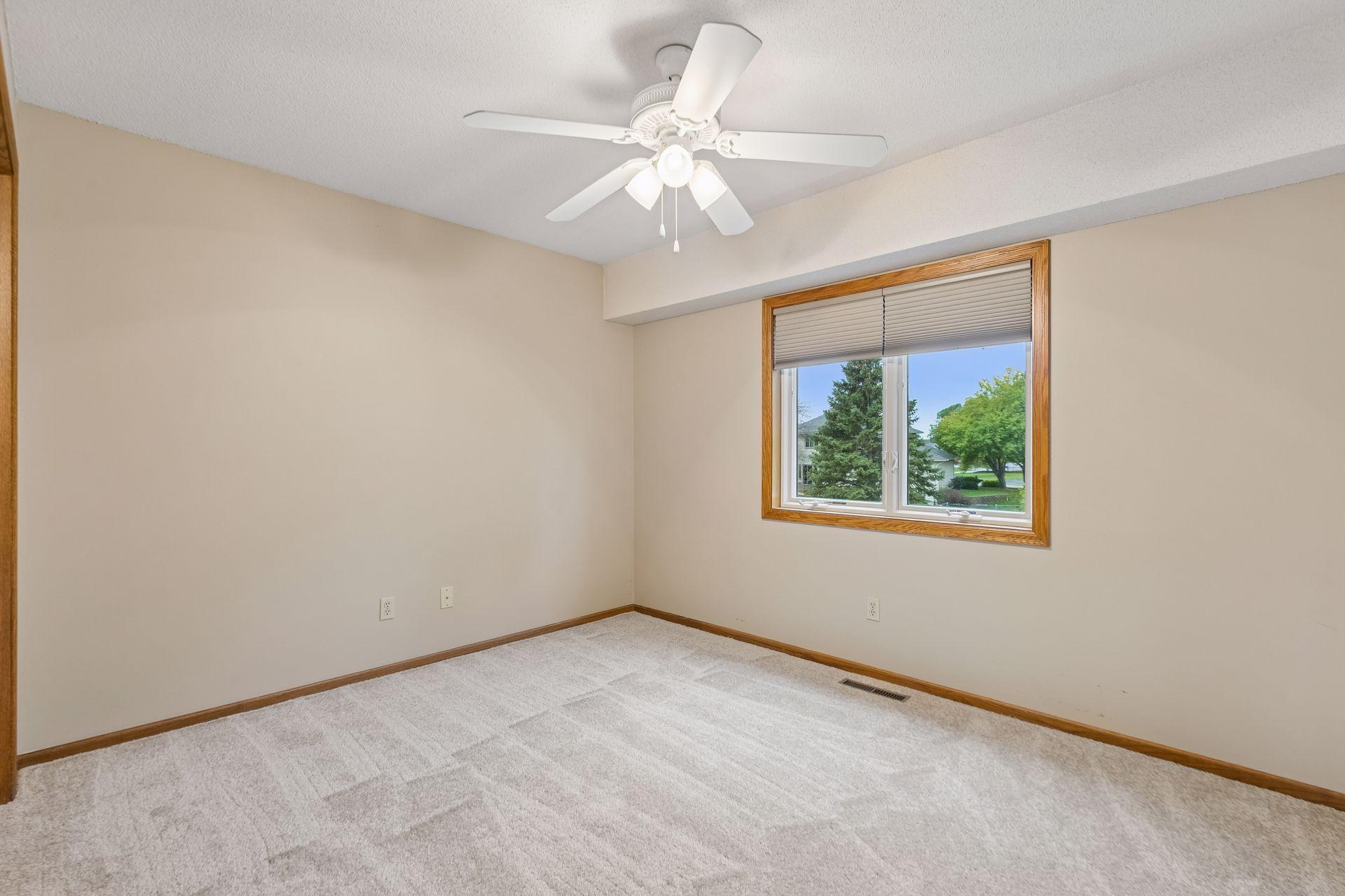 Empty carpeted bedroom with a ceiling fan and a wood-trimmed window.