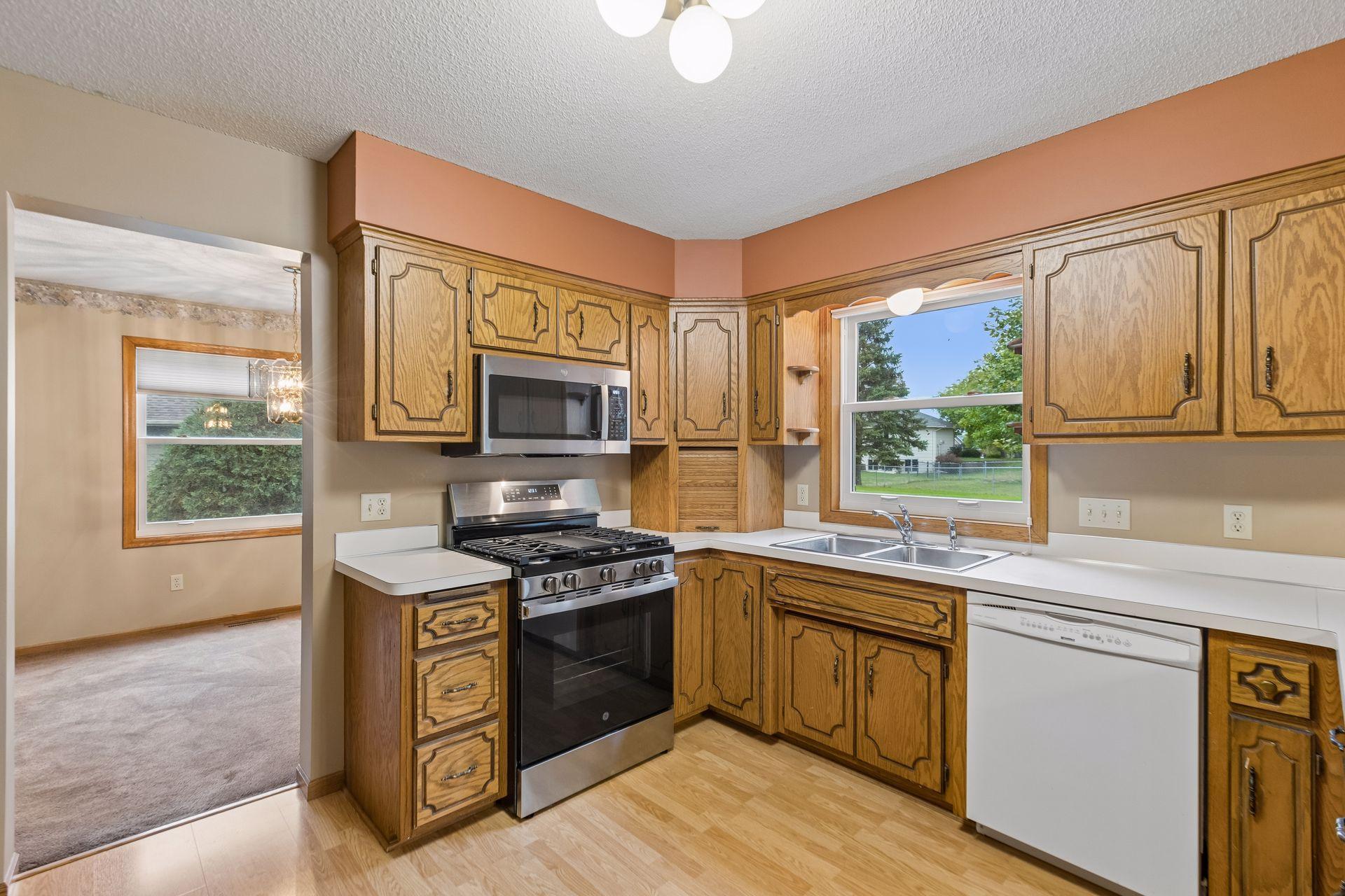 Kitchen with honey-colored cabinets, stainless steel appliances, and a double sink beneath a window.