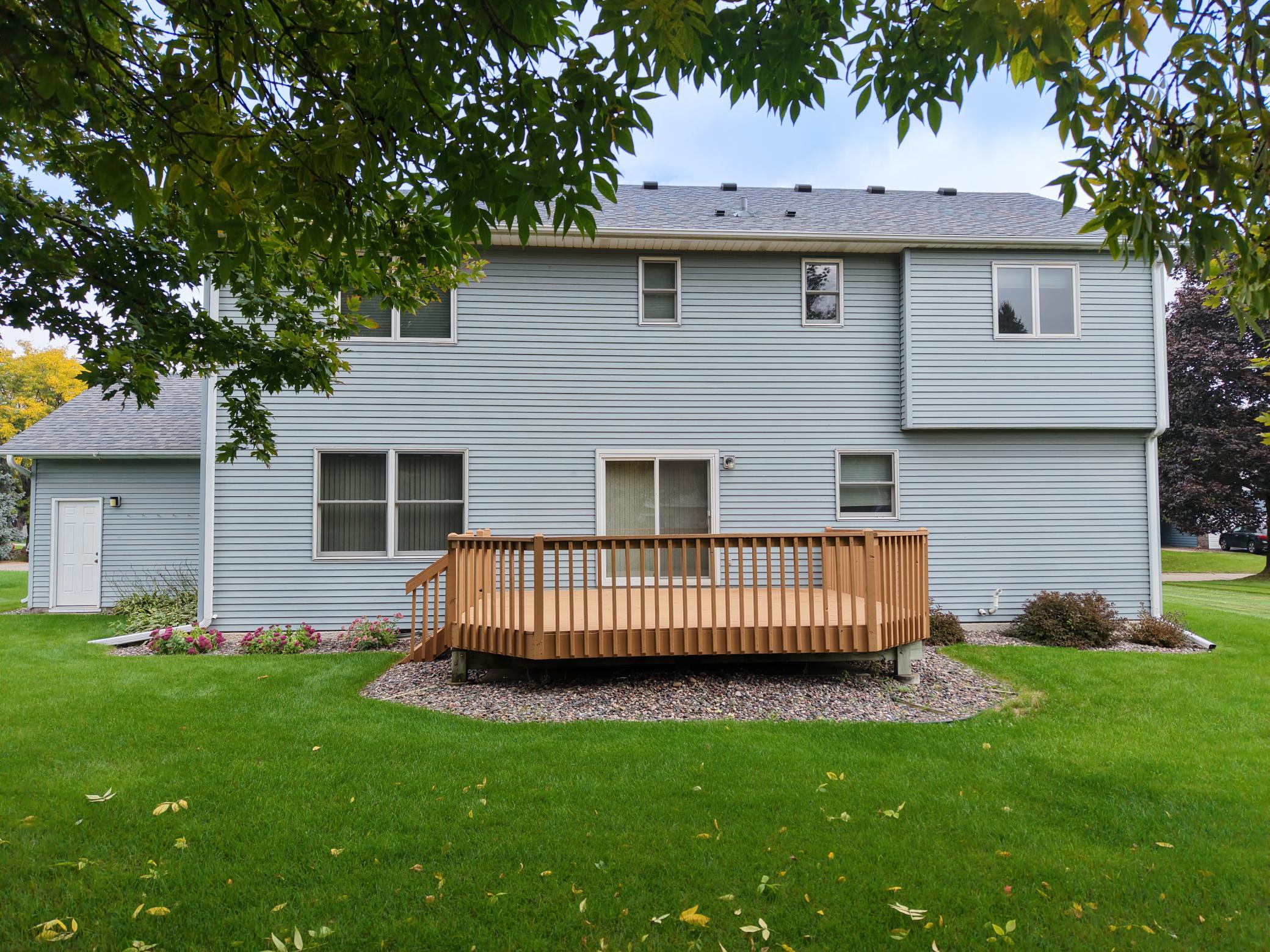 Rear of a light blue two-story house with a raised wooden deck and broad lawn.