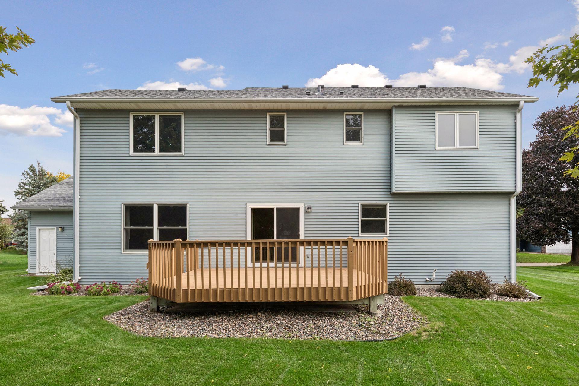 Rear of a light blue two-story house with a raised wooden deck and landscaped lawn.