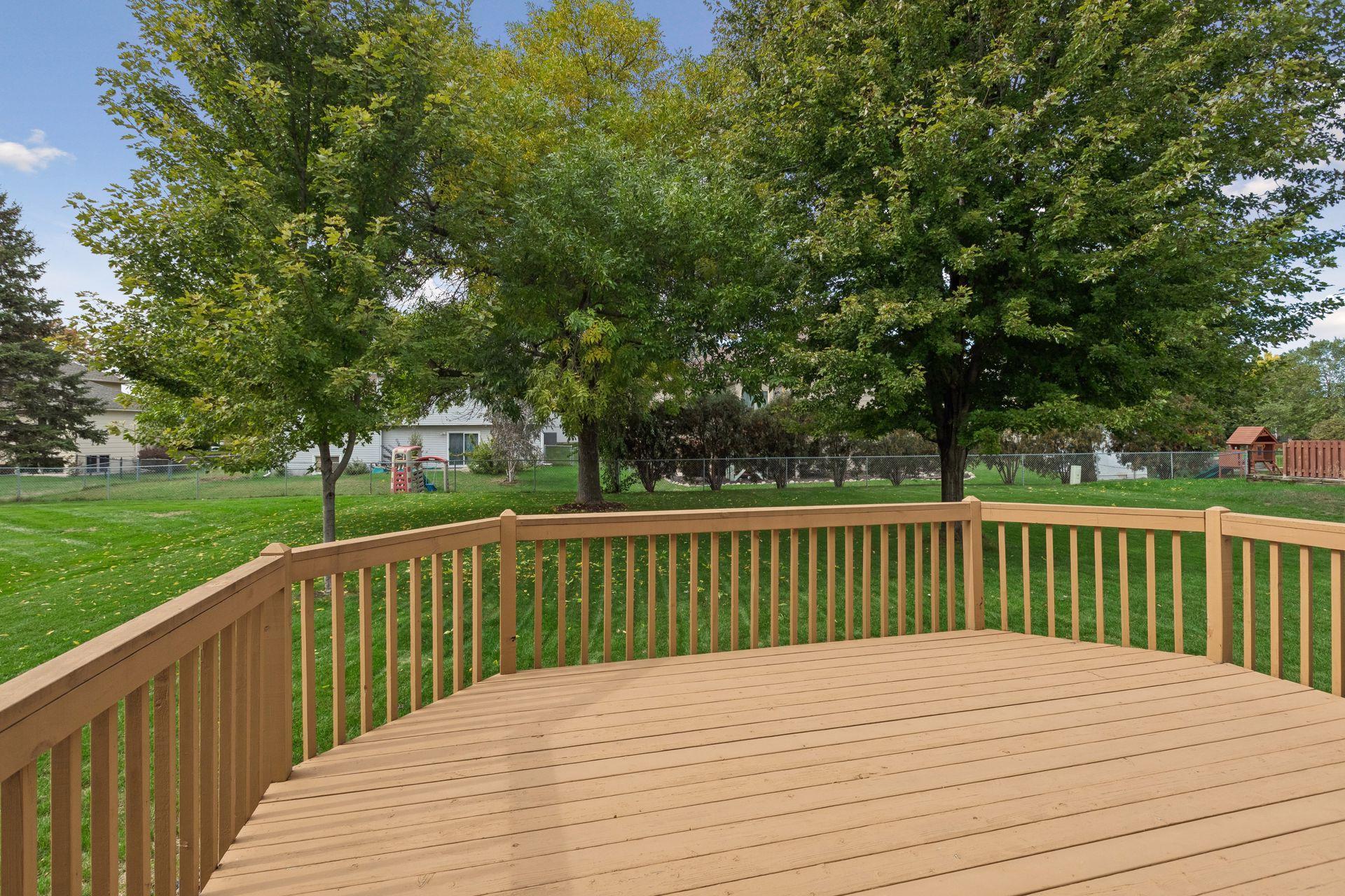 Wooden deck overlooking a leafy backyard with a fenced lawn and mature trees.