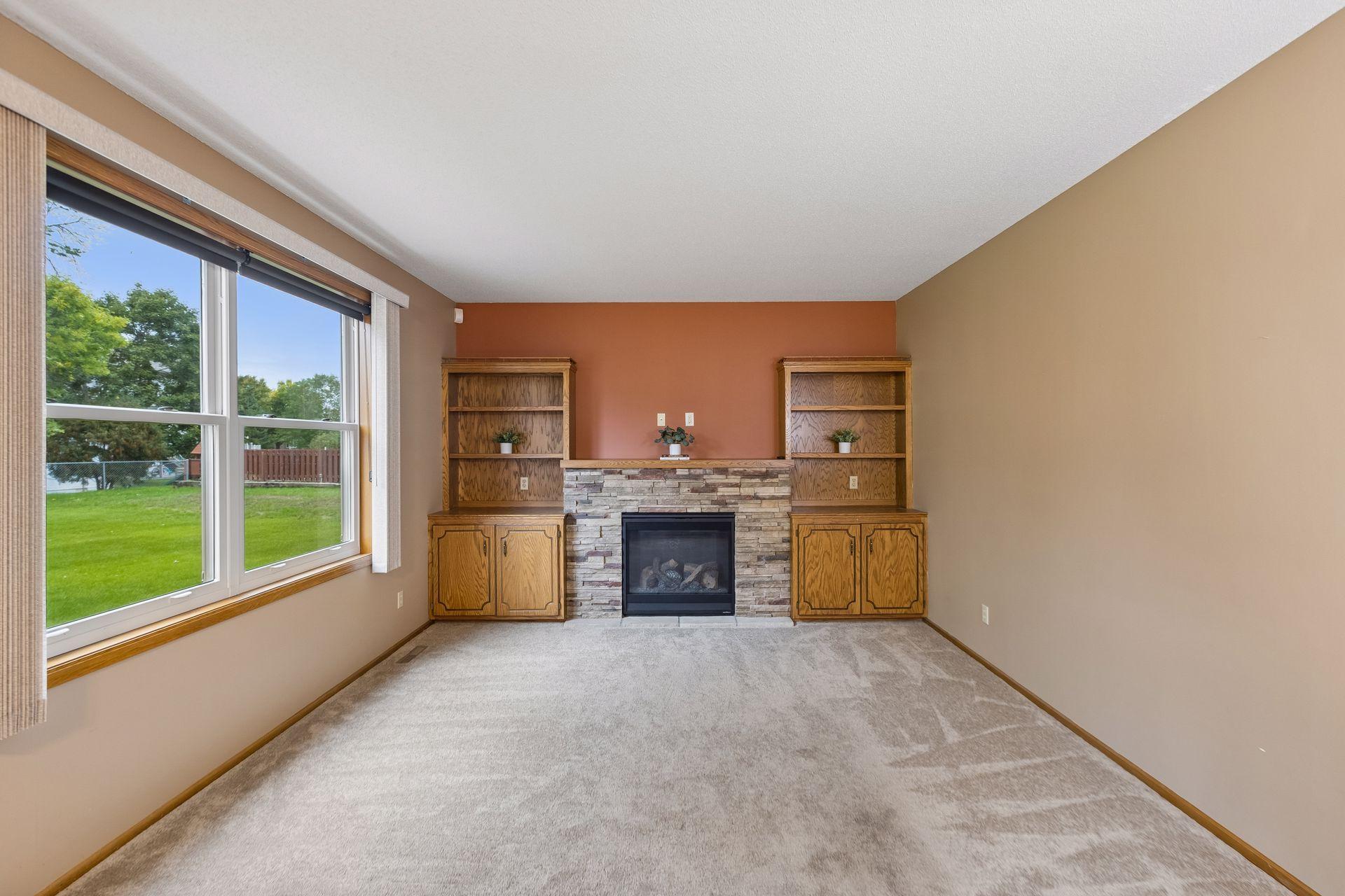 Living room with a stone fireplace, built-in wood shelving, and a large window facing the yard.