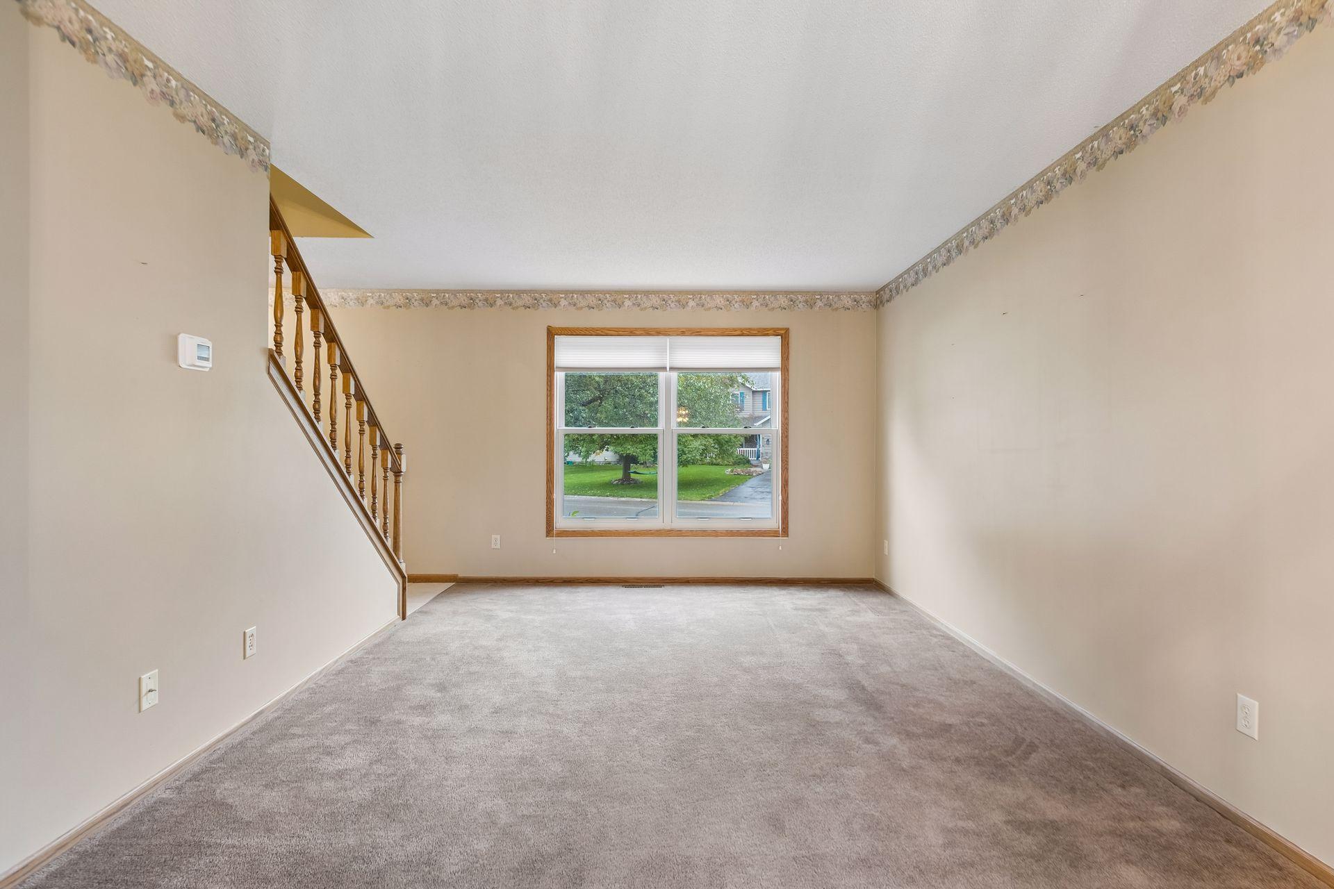 Empty carpeted living room with a wooden staircase and a large window.