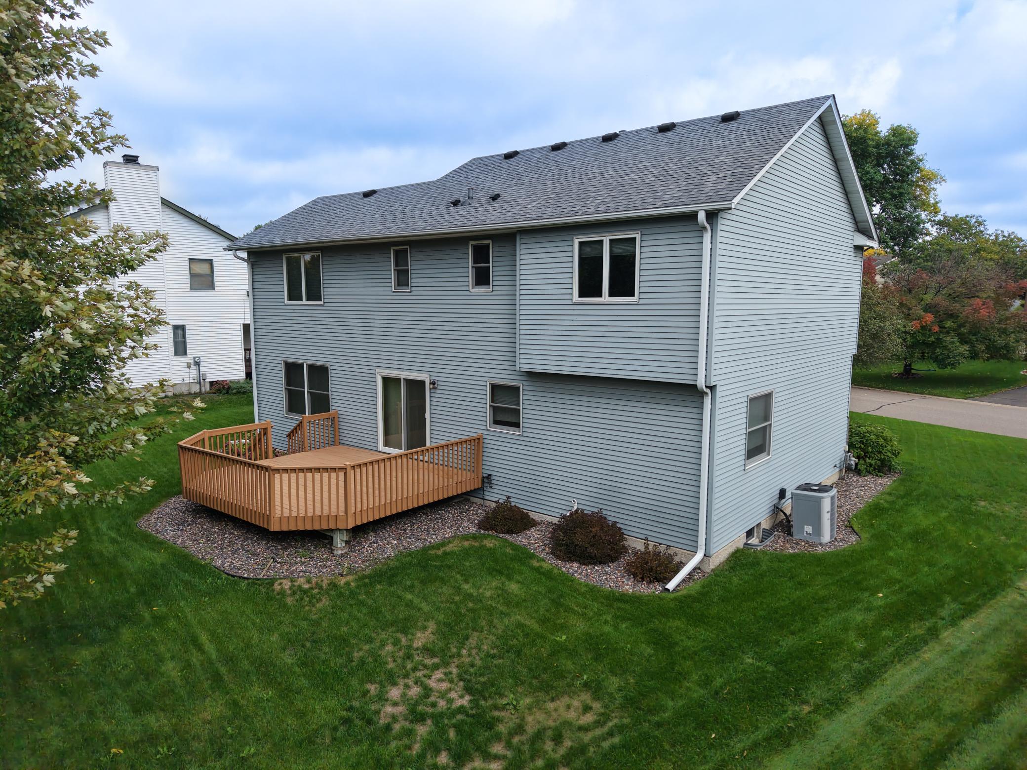 Gray two-story house with a raised wooden deck overlooking a broad backyard lawn.
