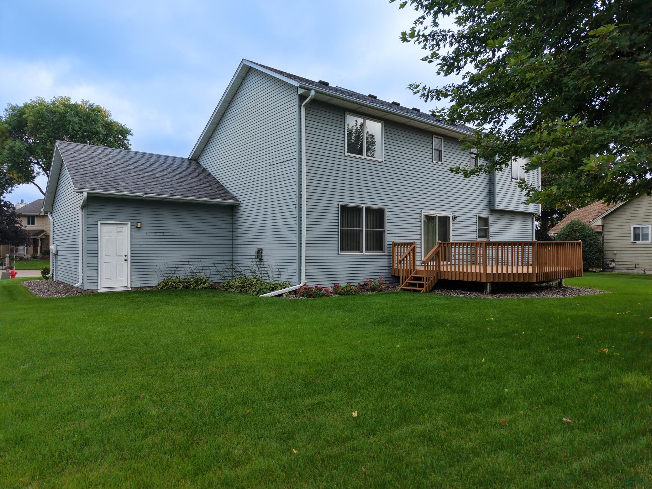 Rear of a blue-gray two-story home with a raised wooden deck and broad green lawn.