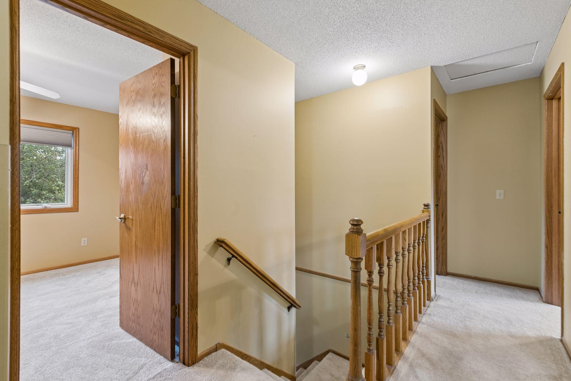 Carpeted upstairs hallway with a wooden stair railing and an open doorway to a windowed room.