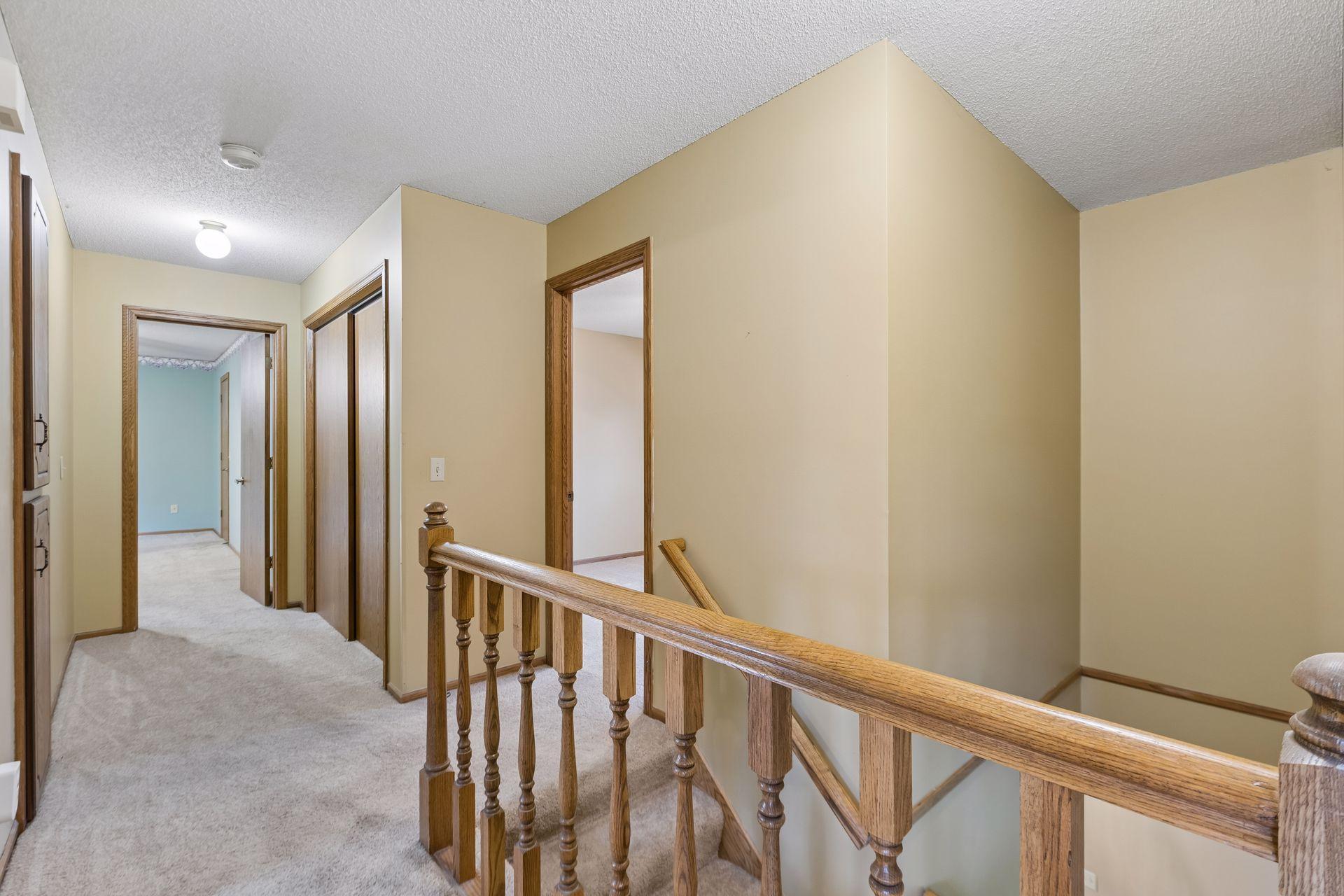 Carpeted upstairs hallway and stair landing with a wooden railing and blue room beyond.