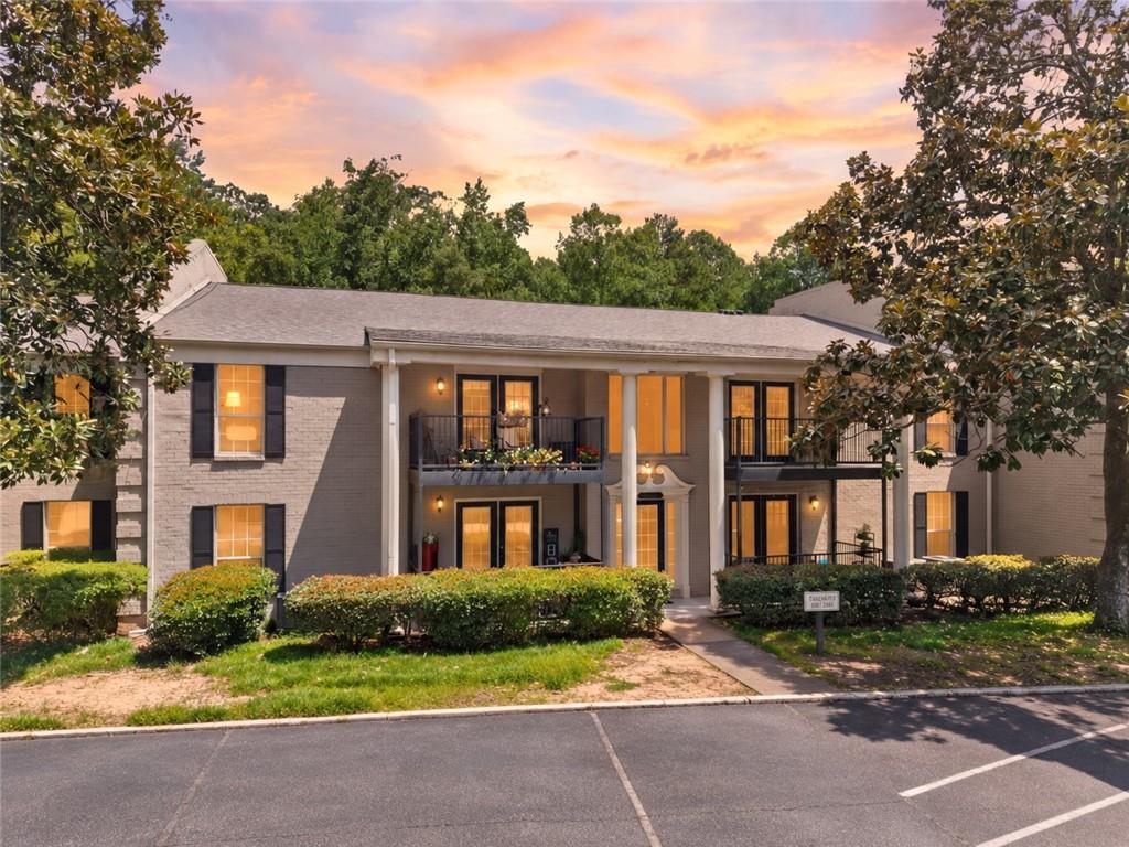 Two-story brick residential building with balconies and lit windows at sunset.