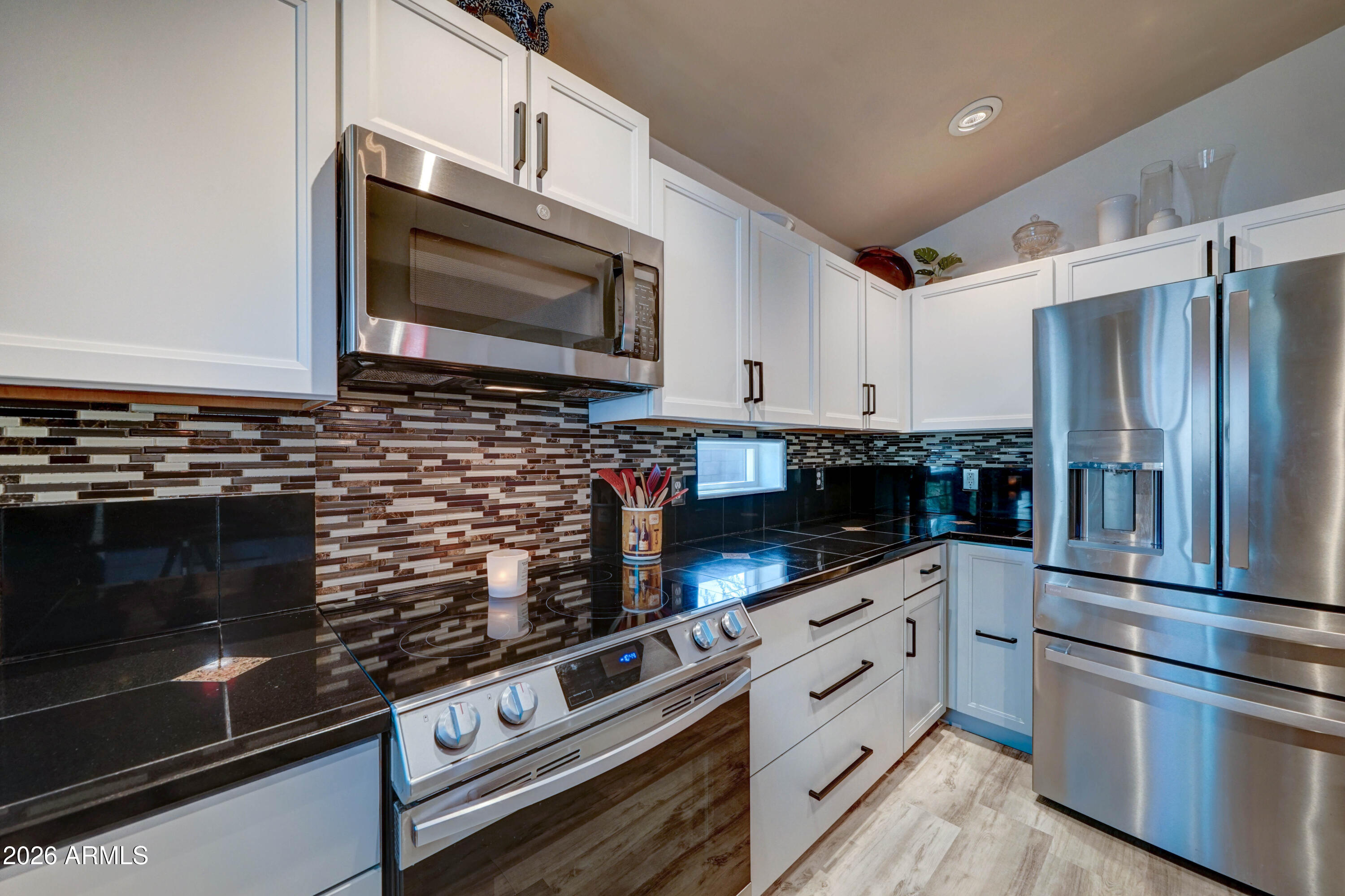 Kitchen with white shaker cabinets, black countertops, mosaic backsplash, and stainless steel appliances.