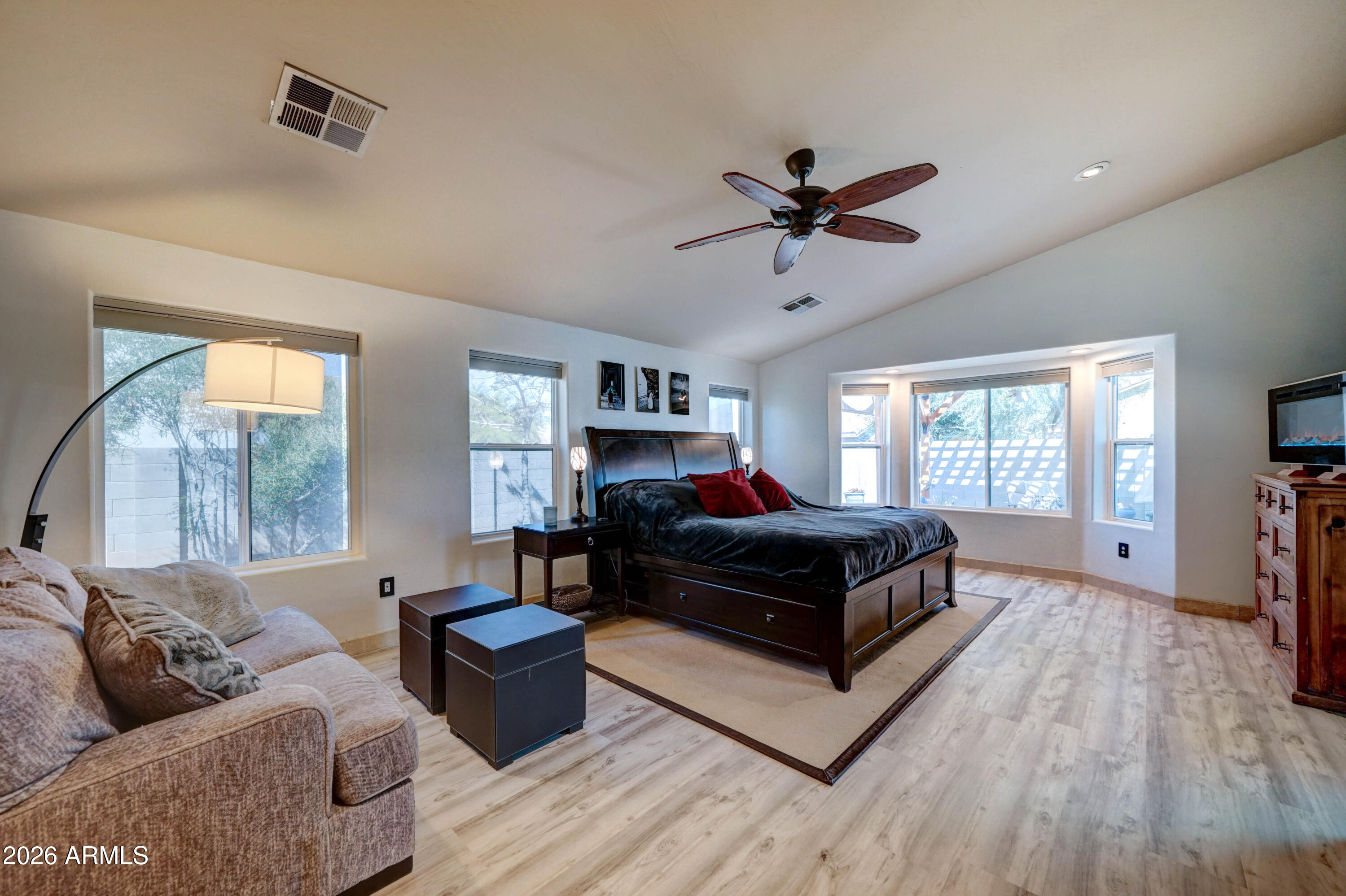 Furnished bedroom with dark wood bed, beige sofa, and a bright bay of windows.