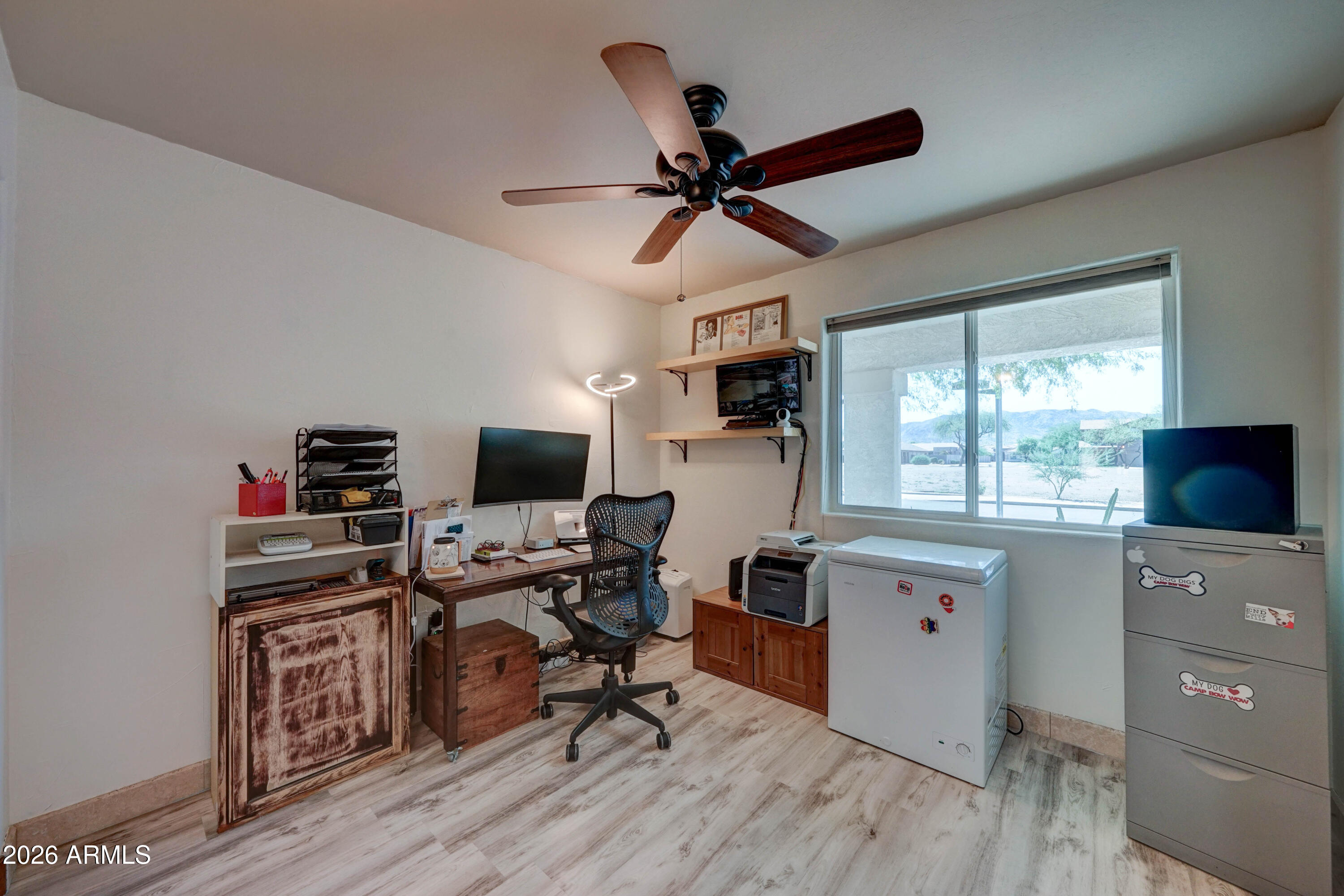 Home office with a workstation, chest freezer, ceiling fan, and large window overlooking distant hills.