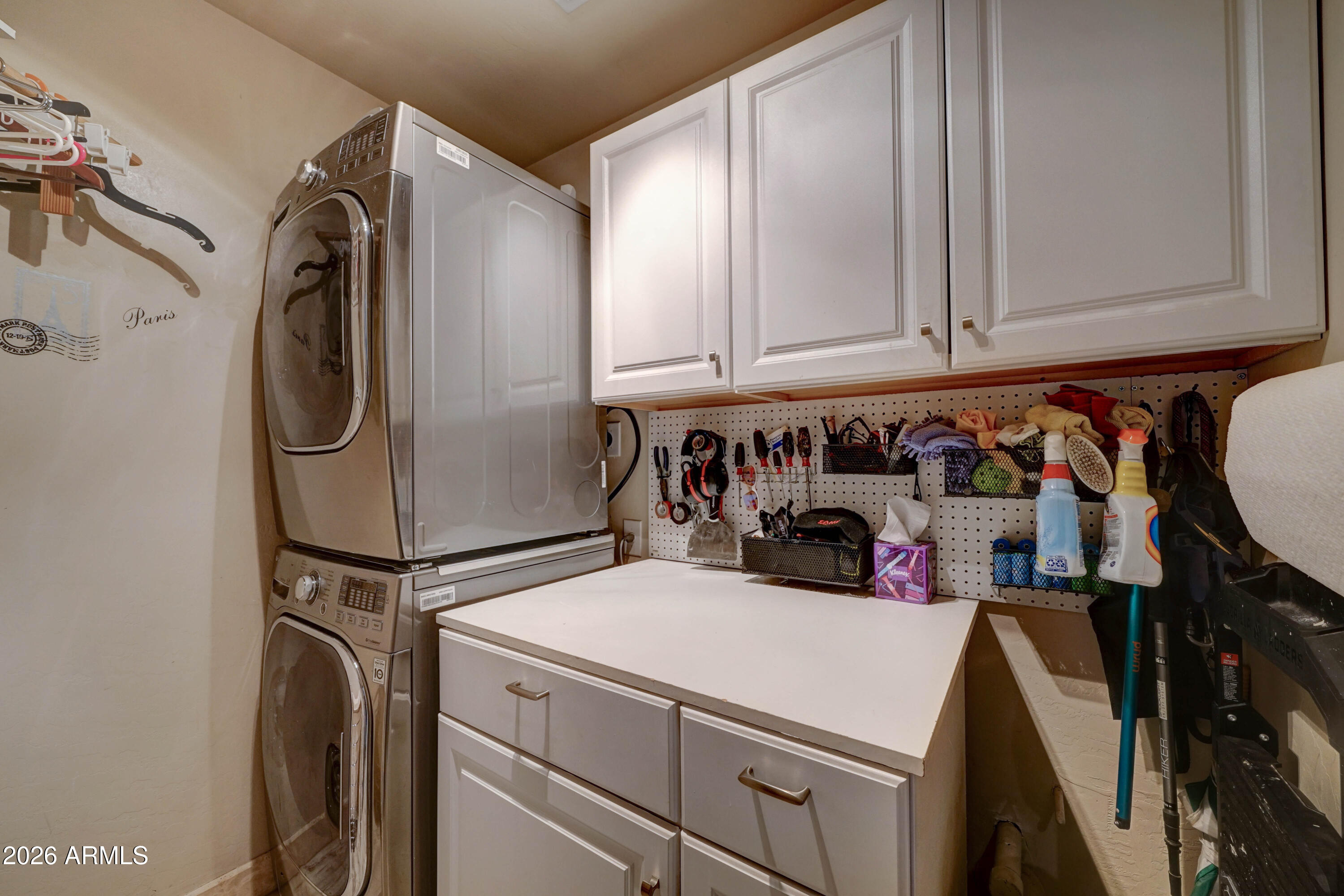 Laundry room with stacked washer and dryer, white cabinets, a work counter, and organized tool storage.