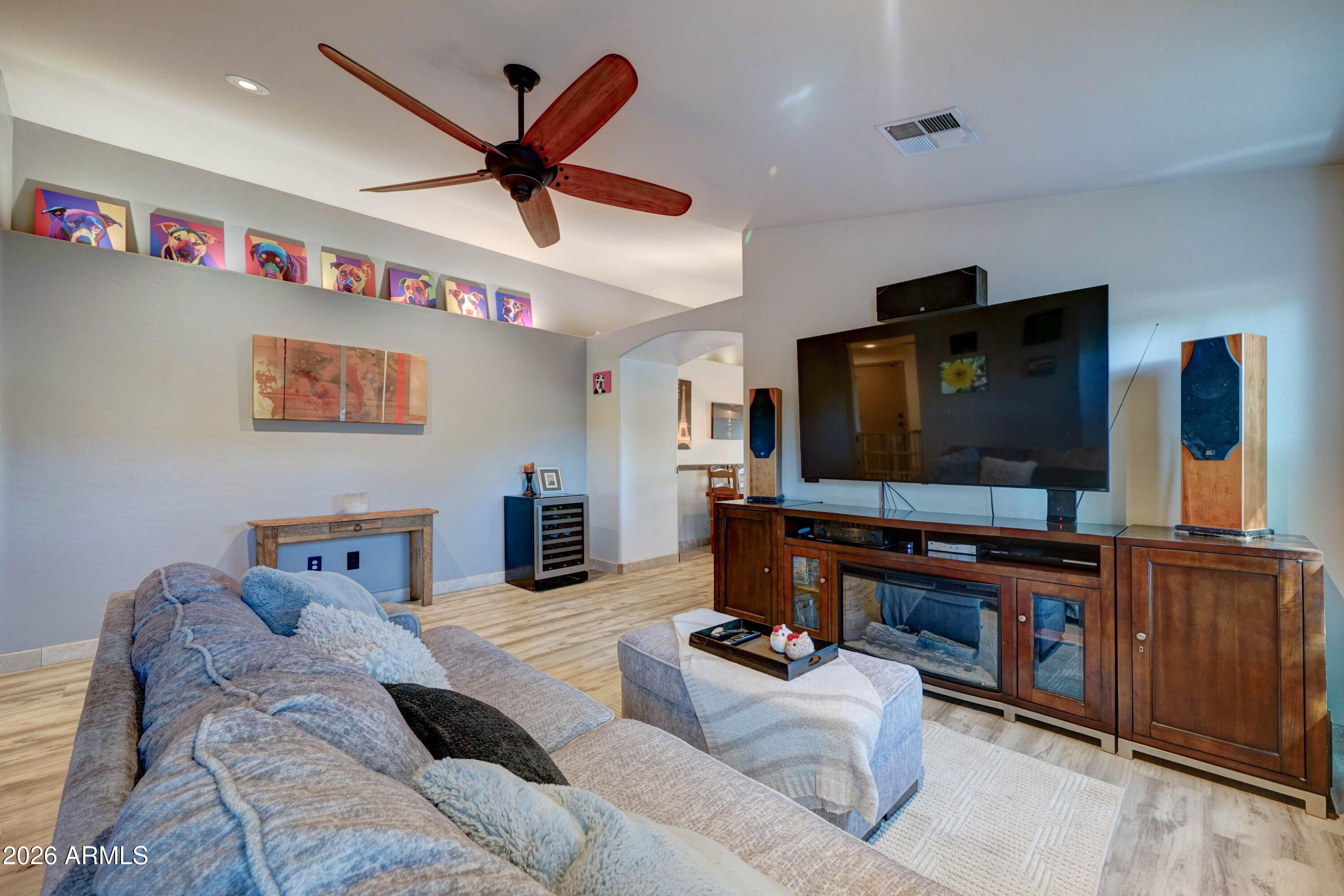 Living room with a gray sectional, large television, wood media console, and colorful dog portraits.