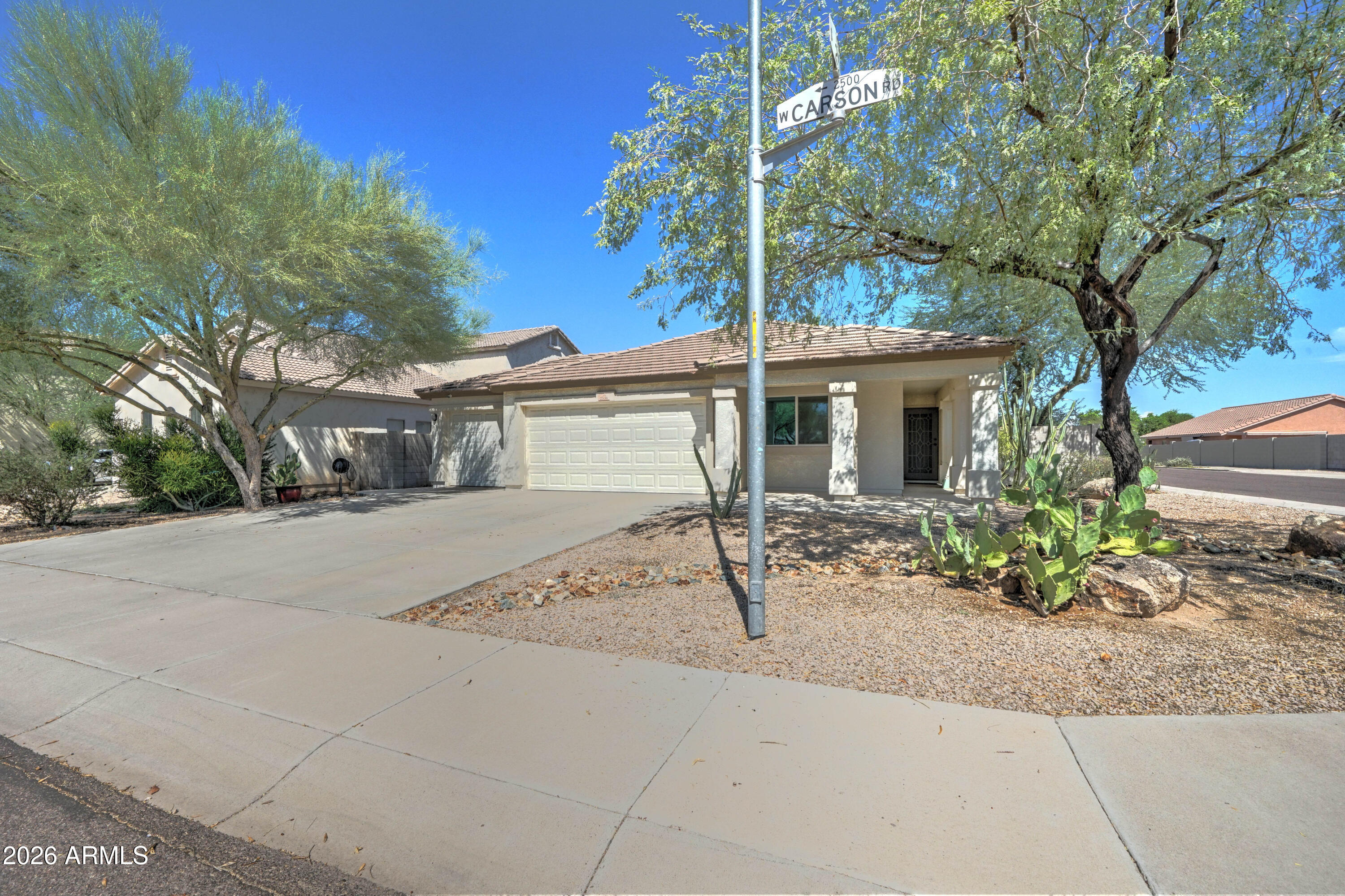 Single-story stucco home with a two-car garage, desert landscaping, and a W Carson Road street sign.