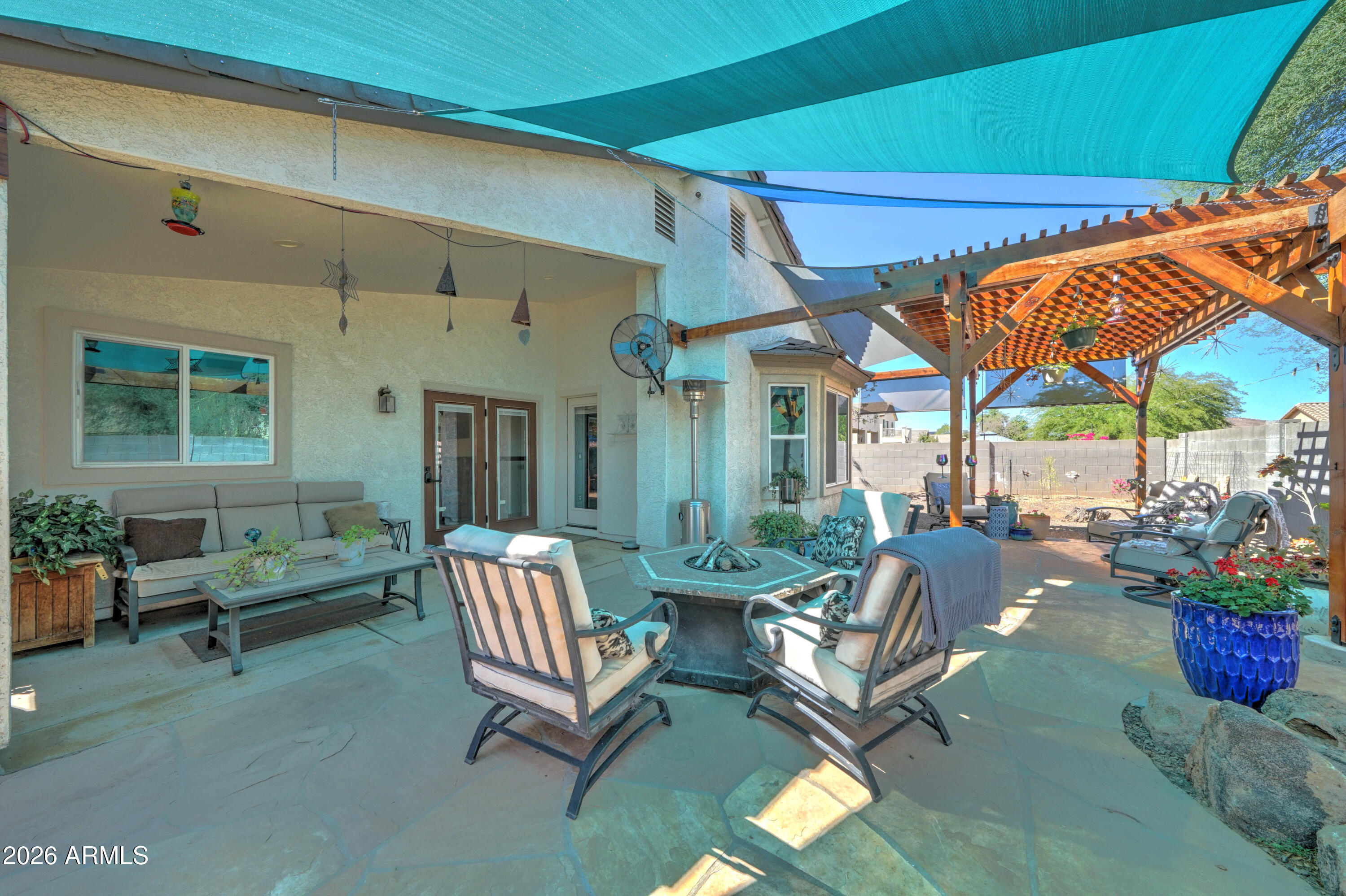 Backyard patio with a fire pit, cushioned seating, wooden pergola, and turquoise shade sails.