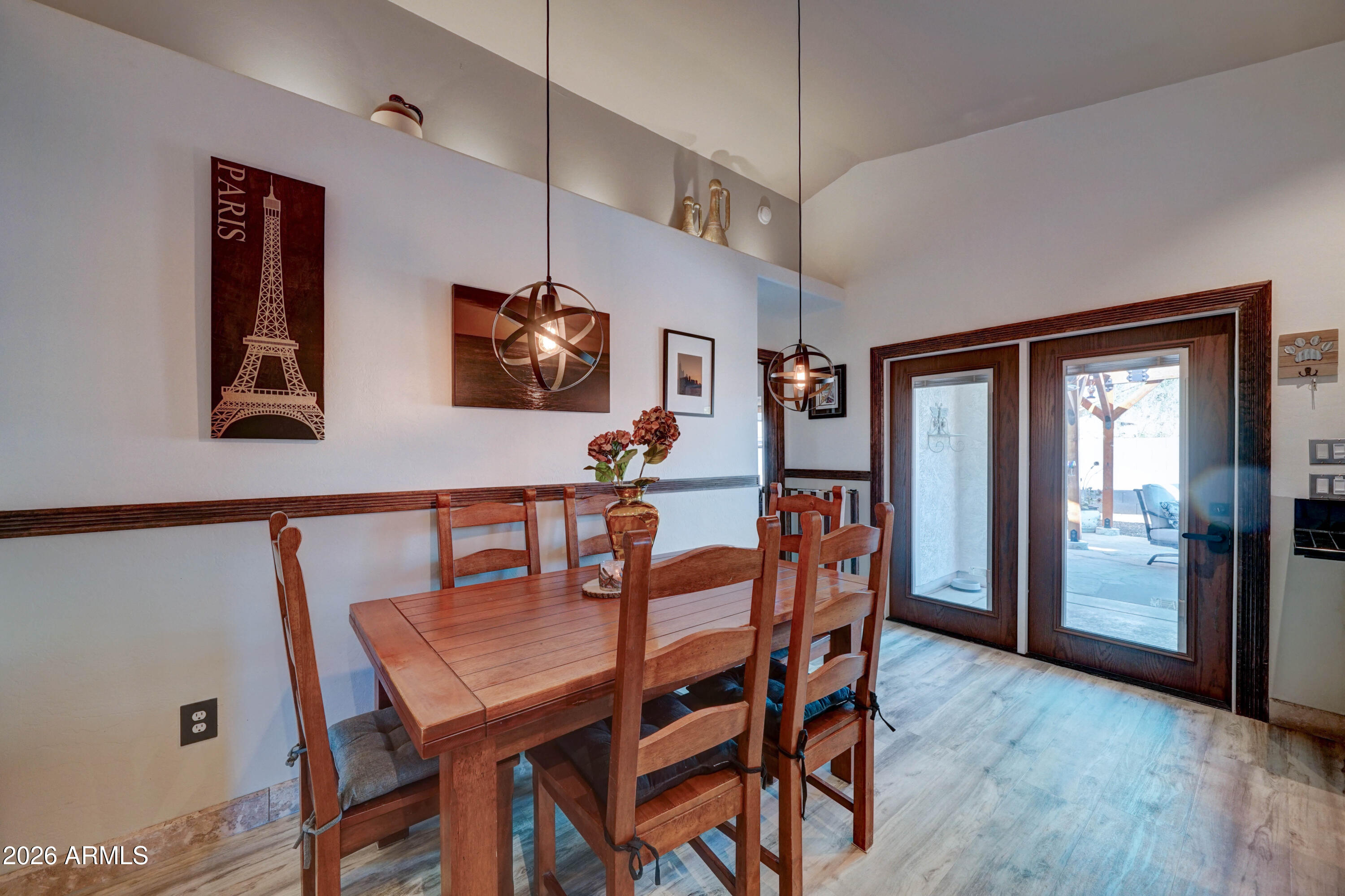 Dining room with a wooden table, pendant lights, and dark-trimmed glass doors opening to a patio.