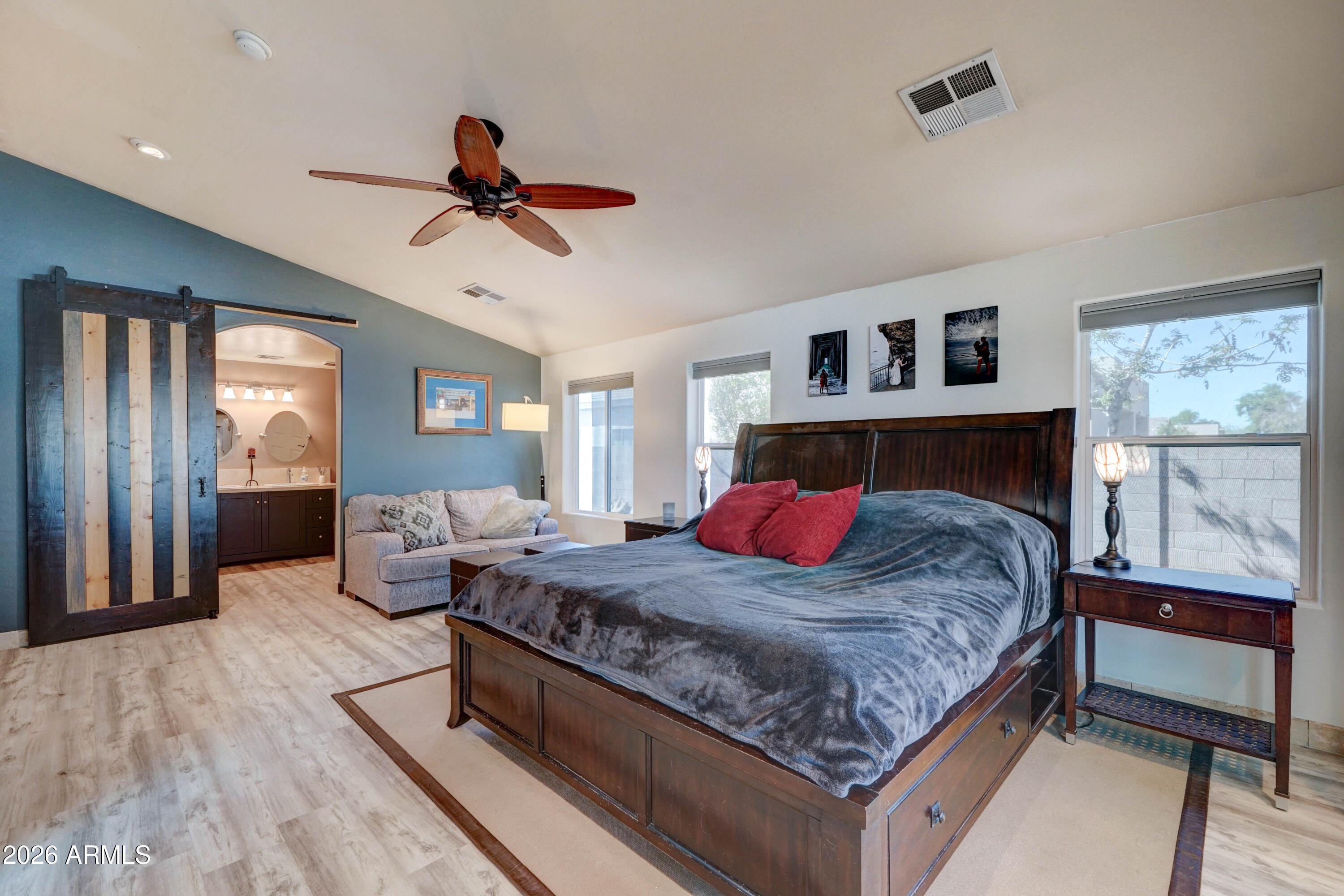 Primary bedroom with a dark wood bed, red pillows, ceiling fan, and sliding barn door.