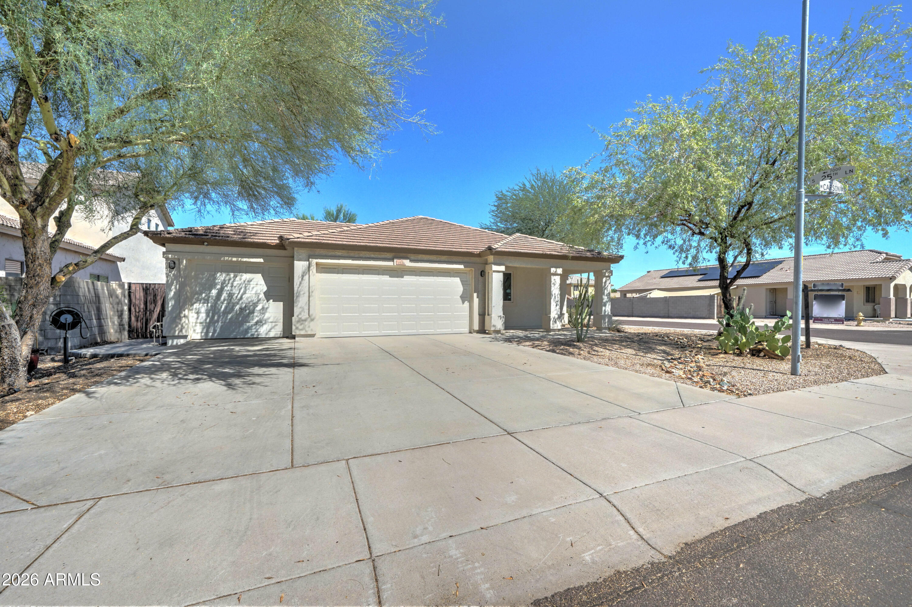 Single-story home with a broad driveway, double garage, tile roof, and desert landscaping.