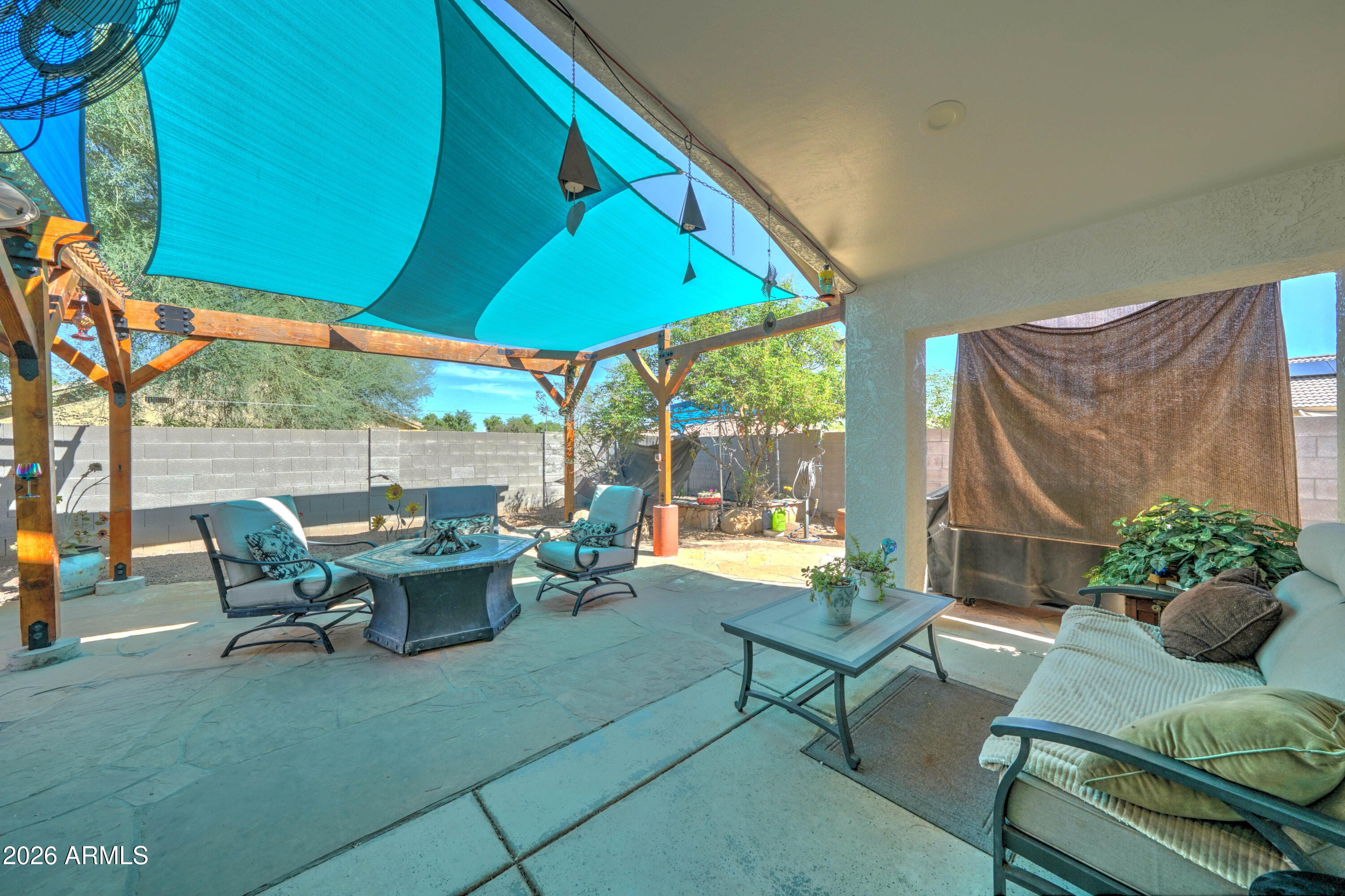 Covered backyard patio with turquoise shade sails, wooden pergola, and outdoor lounge seating.