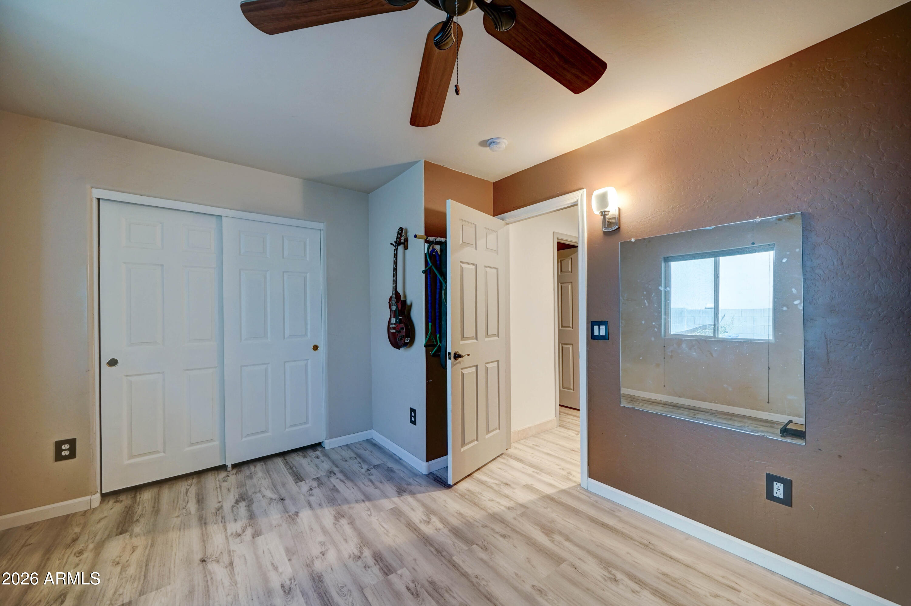 Empty bedroom with sliding closet doors, a ceiling fan, and a large wall mirror.
