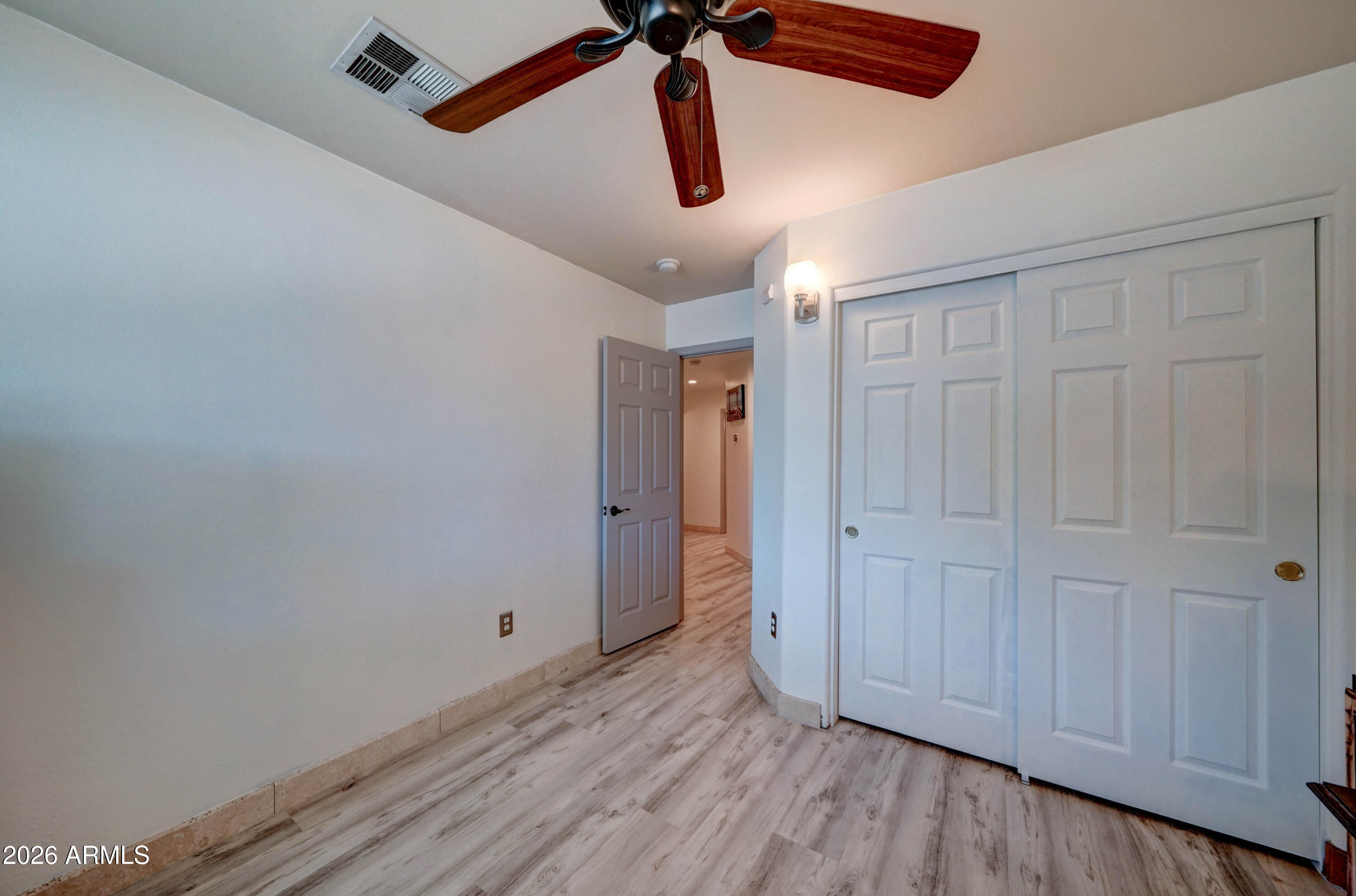Empty bedroom with wood-look flooring, a ceiling fan, and large sliding closet doors.