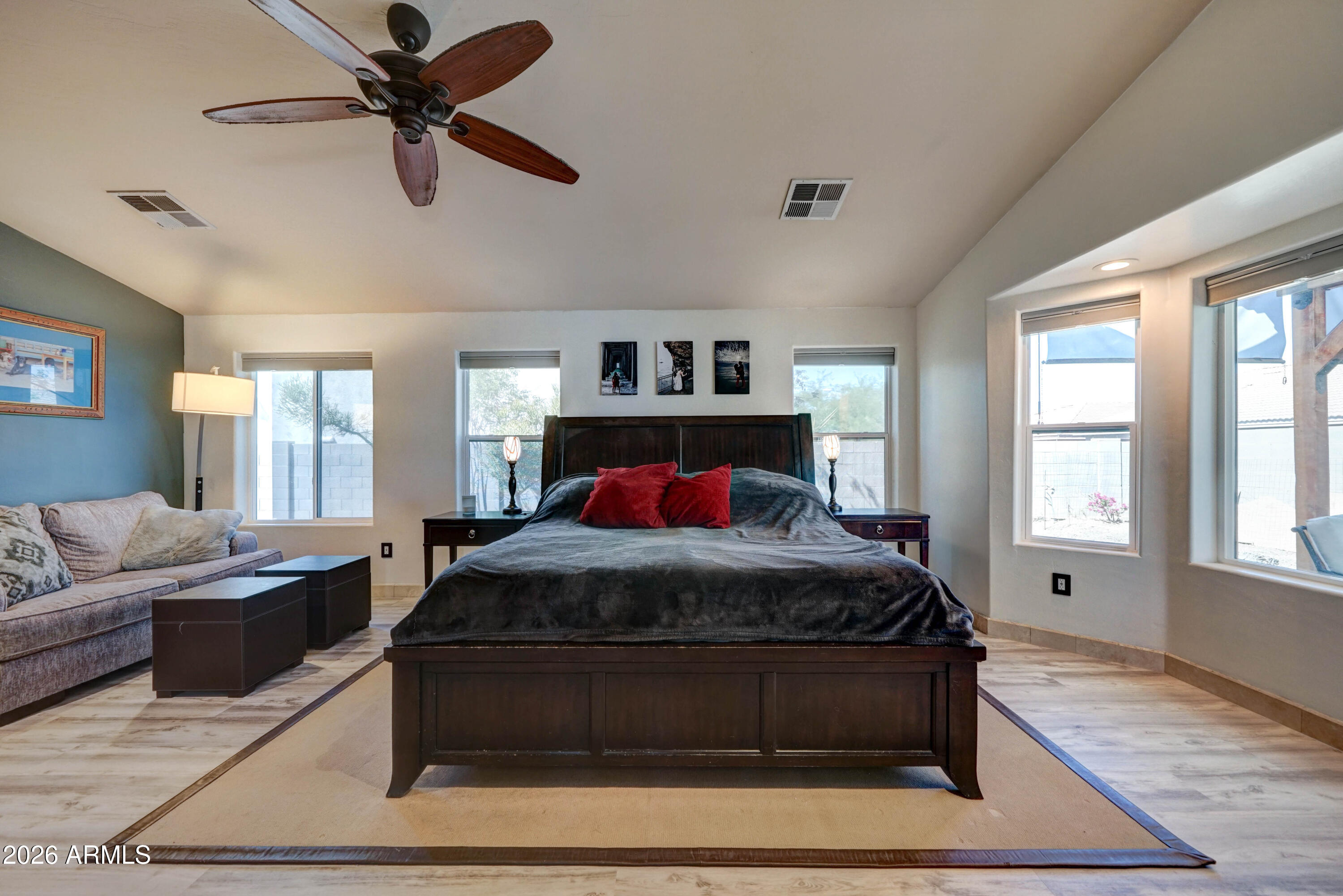 Furnished bedroom with a large dark wood bed, red pillows, a ceiling fan, and a sofa seating area.