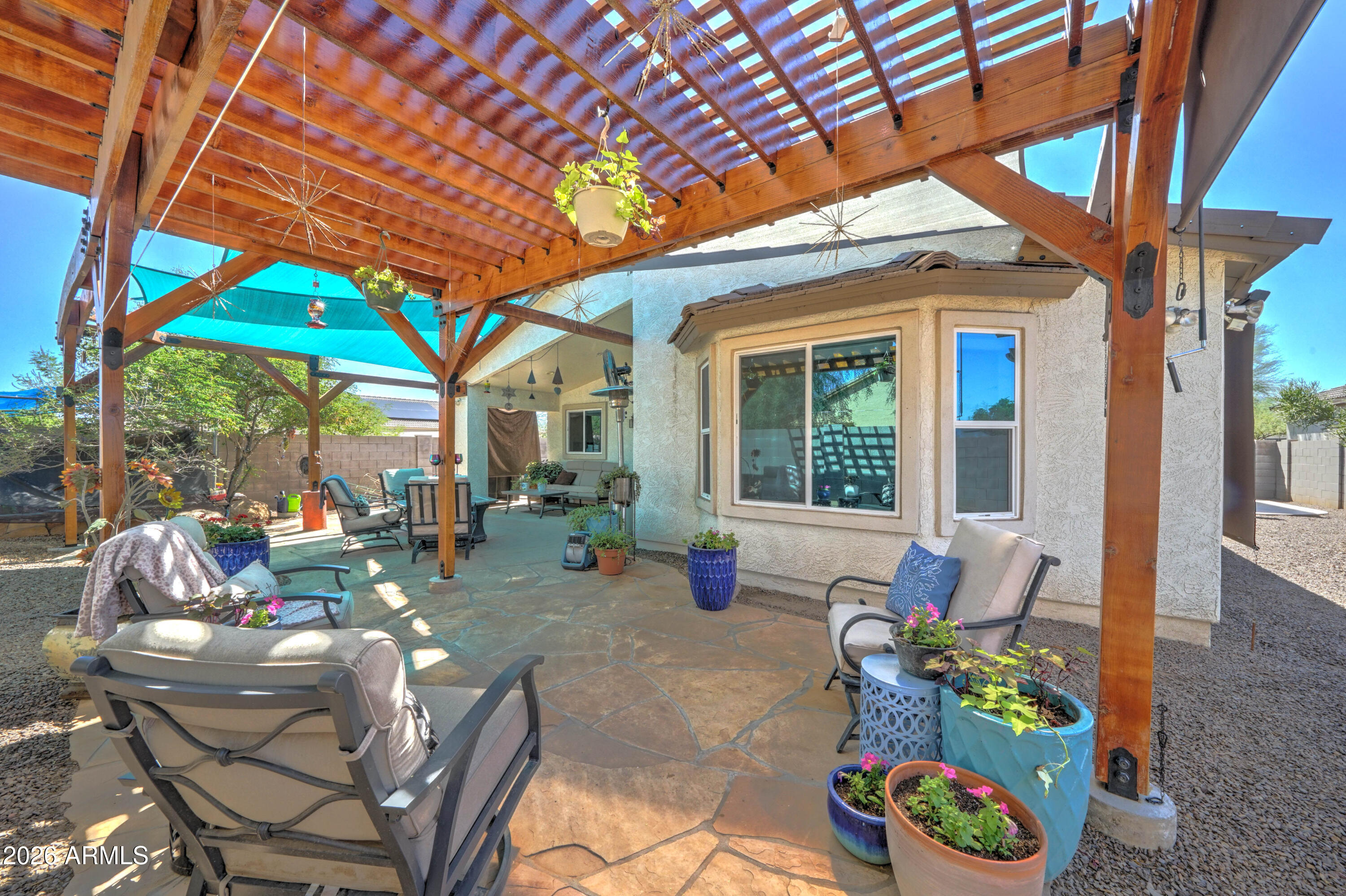Backyard patio with stone paving, lounge chairs, potted flowers and a wooden pergola.