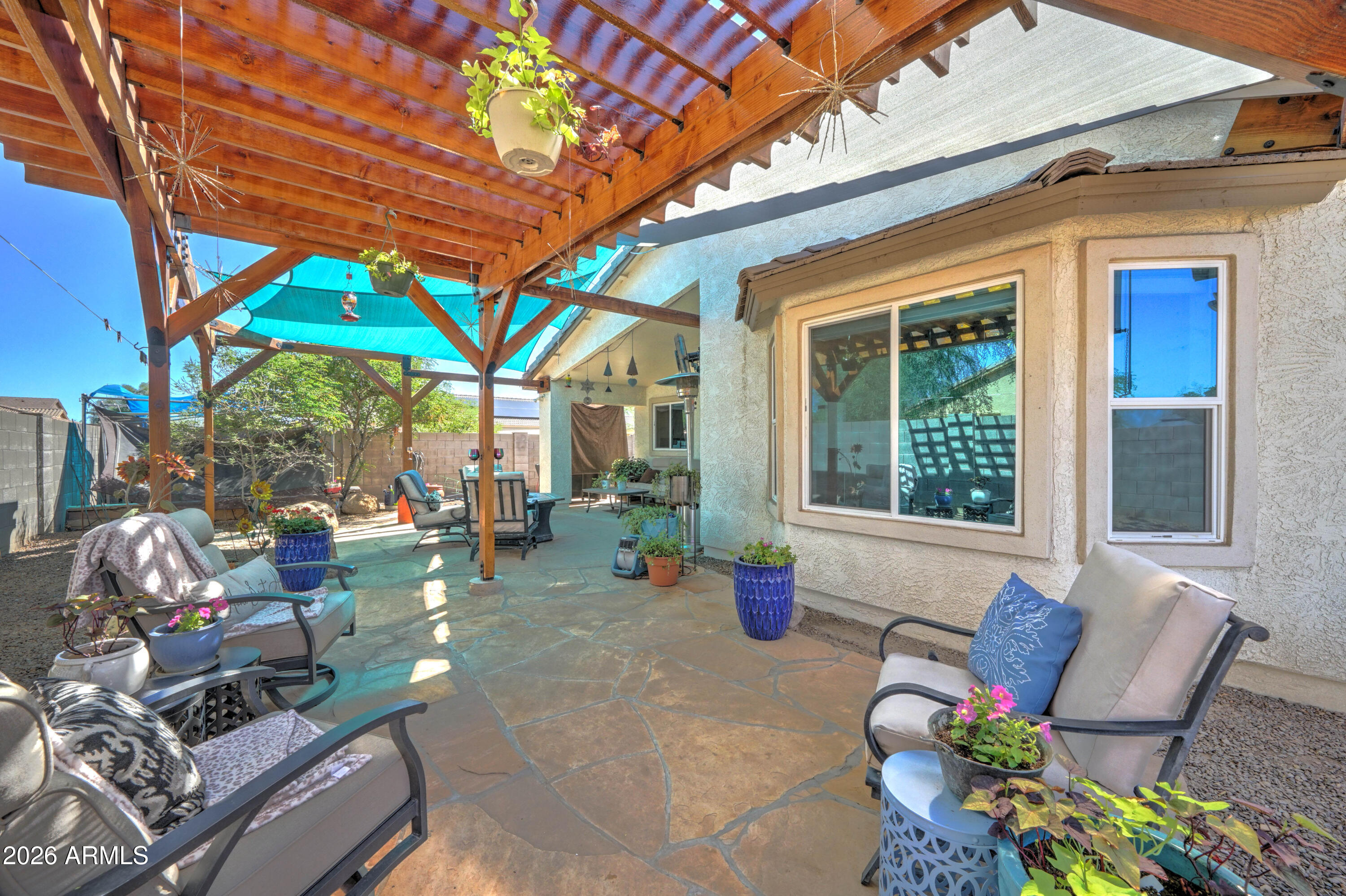 Furnished flagstone patio beneath a wooden pergola with turquoise shade cloth and potted plants.
