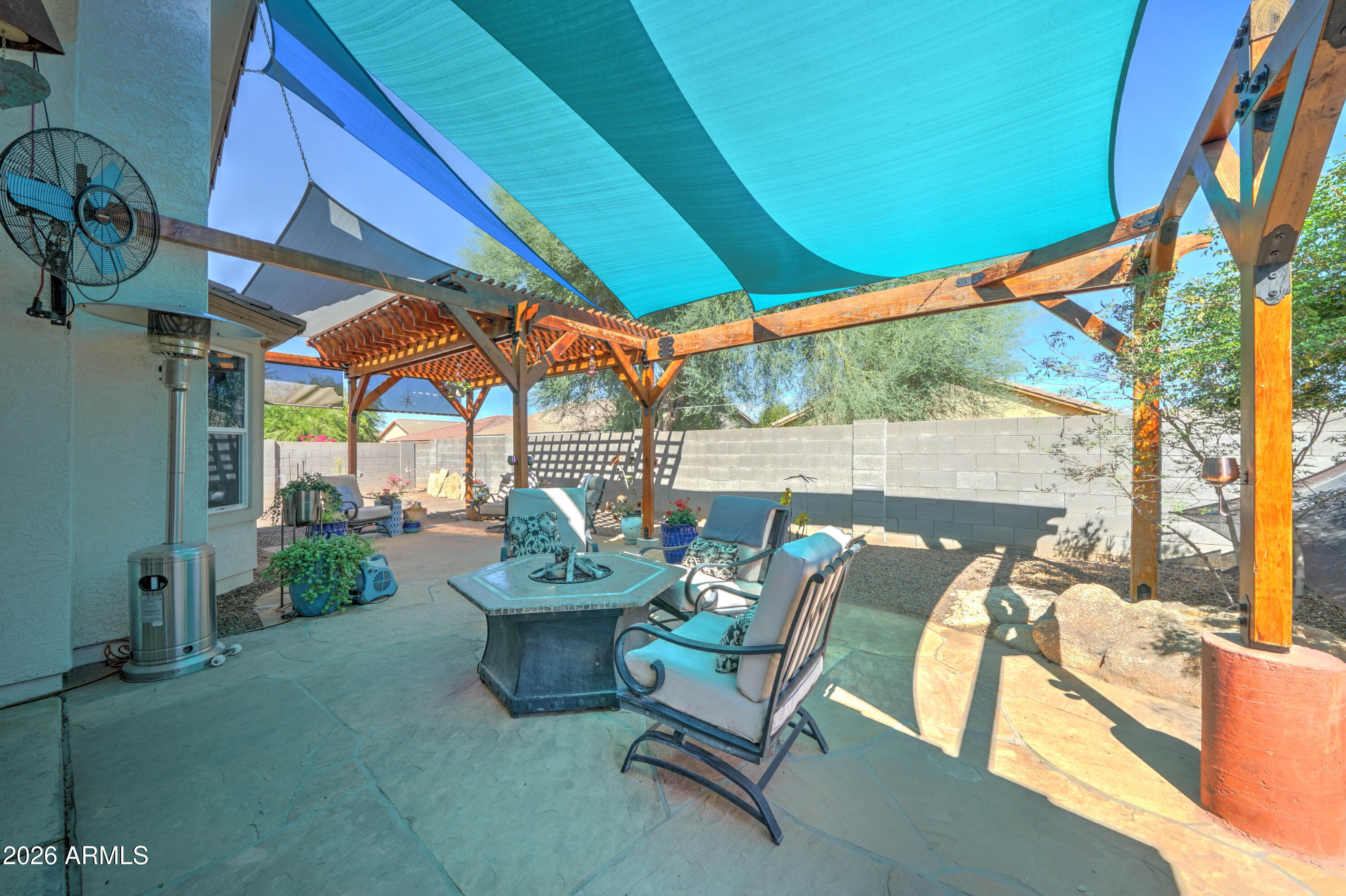Backyard patio with shade sails, a wooden pergola, and seating around a fire table.