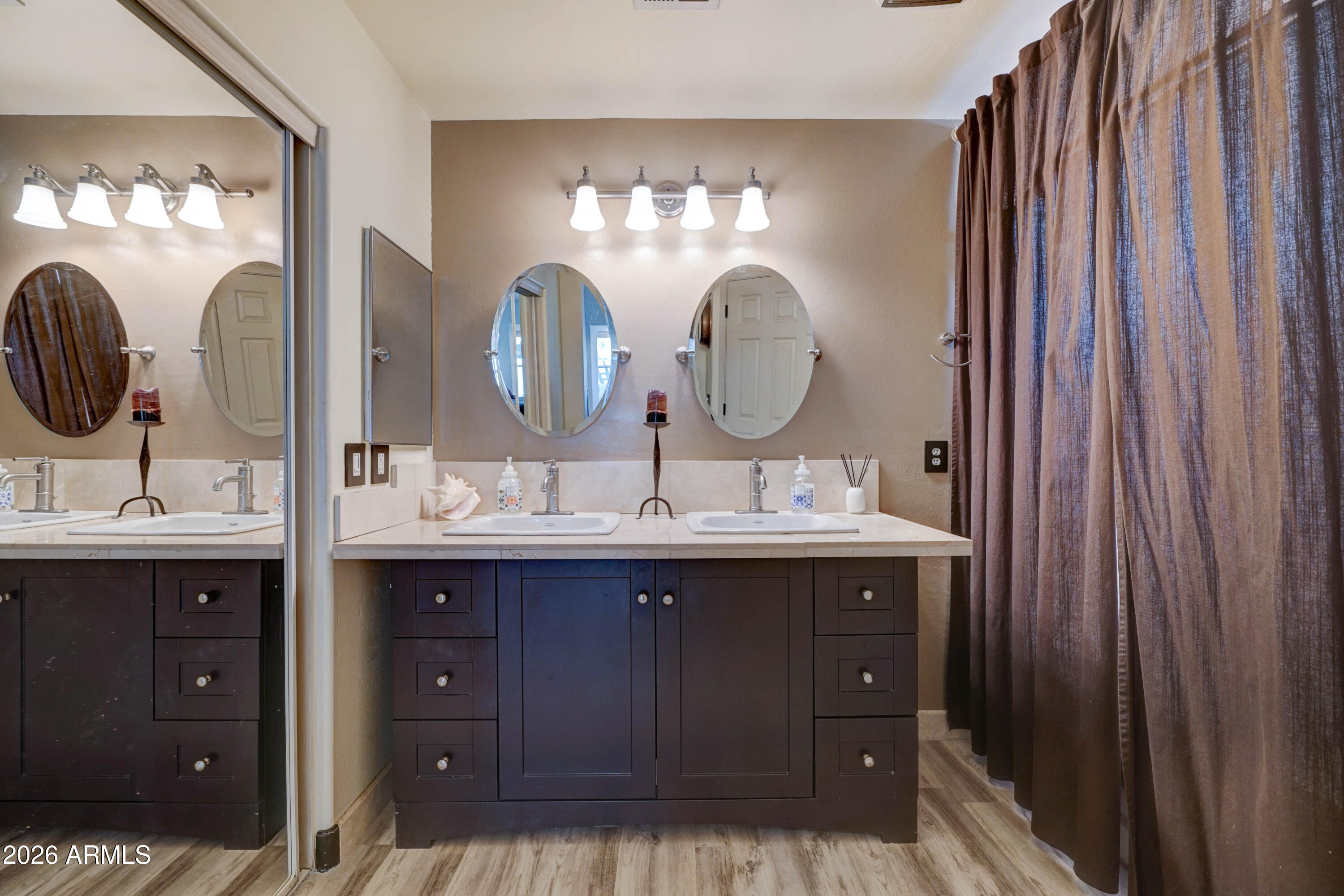 Bathroom with a double-sink vanity, dark cabinetry, oval mirrors, and a floor-length shower curtain.