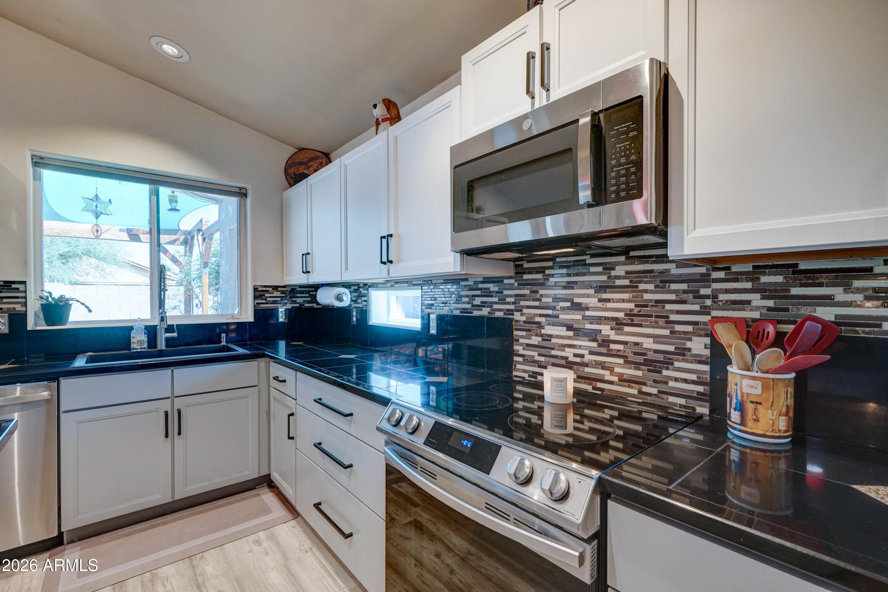 Kitchen with white cabinets, black counters, stainless steel appliances, and a mosaic tile backsplash.